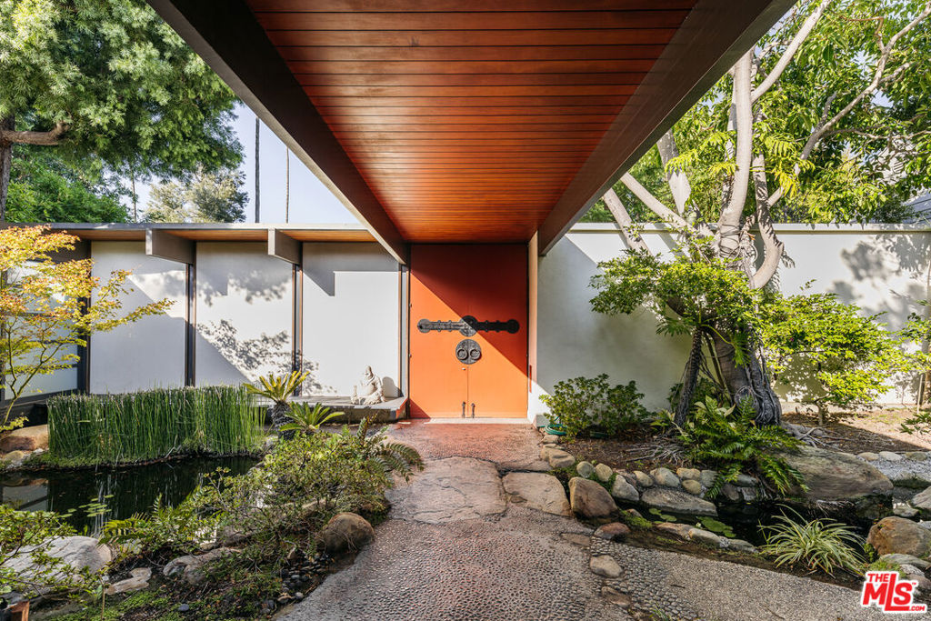 Transcend into zen opulence in this stunningly preserved mid-century Japanese Minka on an expansive lot in the heart of Beverly Hills. Designed in 1960 by Jack A. Charney, known internationally for his iconic Sierra Towers building, 703 N Canon offers 7,500 square feet of awe-inspiring interior living space. With six en suite bedrooms and a multifunctional upper-level loft, the floor plan contrasts traditional Japanese forms with a vernacular that is firmly modern. Enter the circle driveway where clean lines and period hardware beckon you inside. A serene garden courtyard sets a tranquil tone with cascading koi pond and contemplative landscaping. Off the entry, a formal living room with suspended mantle fireplace, exposed wood beamed ceiling, and shoji screens open to reveal calming views to the garden. A chef-worthy kitchen boasts a large center island, stainless steel appliances, and breakfast nook. The adjacent formal dining room provides the perfect gourmet setting, complemented by wine stored in the secure cellar and tasting room. Make your way to the lounge and family room, where a sunken bar with and Capiz light fixtures radiate 1960s Hollywood glamour. A double-sided fireplace connects to the home library with serene vistas to the atrium. On the main level, the north wing features hand carved skylight screens throughout the hallway, leading to six en suite bedrooms - each with outdoor access and ample closet space. Enter the luxurious primary suite accented with gilded wallpaper and built-in bench seating. Continue to the spa-inspired bathroom adorned with wood cabinetry, and paneled ceiling. In the backyard, a majestic, outdoor paradise unfolds to reveal a Cyprus-shaped pool, stone walkways, and lush lawn spaces. A tranquil pond surrounds the outdoor dining area and quintessential Japanese tea house. At the rear of the property, a meditation room is a welcome retreat from the stresses of modern life. 703 N. Canon is a true mid-century dream, lovingly preserved and proximate to the very best of Beverly Hills.