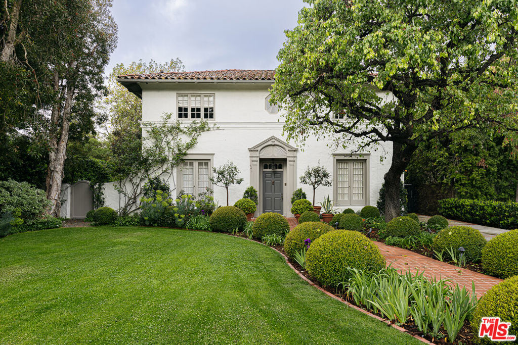 Built in 1922 by famed architect Elmer Grey of The Beverly Hills Hotel, with renovations designed by the legendary Paul R. Williams in 1935, this stately Spanish-style home with traditional elements, brings the best of historic California architecture to Windsor Square. Character filled and timeless, this prestigious home is where Hollywood romance reminiscent of a by-gone era meets a modern escape. Set-back from the street, your heart will soar the moment you arrive to witness the ornamental pear tree beckoning you to a world of lush landscaping and storied pedigree. Meticulously renovated by Tim Barber and interior designer Elizabeth Dinkel, light abounds throughout, reflecting off rich, hardwood floors, welcoming you to an expansive front room complete with handsome fireplace. Move into the enchanting formal dining room with its own pocket doors, separate Butler's pantry with cocktail station and bar sink. Unique single pane window details slide open to allow for a sweet breeze plus a fun party trick as you entertain in the summer. Open-concept kitchen with stainless steel professional-grade Viking appliances, warming oven, wine fridge, center island and custom cabinetry is a true chef's delight. Large finished California basement provides over 500 sq ft of additional usable space for storage and functionality. Enjoy your morning paper in the tasteful living room, perfect for TV watching via your surround sound Home Theater System, reading or simply relaxing with views of the curated garden. The downstairs opens to the backyard off of 4 separate entrances for a true indoor outdoor experience. Wind your way up the stairs via the reverse staircase to the second level where 4 large bedrooms and 3 baths await. The Primary, complete with its own fireplace and dual Juliet balconies, overlooks a serene backyard and rose dotted pergola against a row of magnolia trees. Designer ensuite bath with white marble carrera countertops, separate soaking tub, dual sinks and two large walk-in closets. Separate upstairs Laundry room adds modern convenience. A retreat of tranquility with Zen-like calm abounds as you take in the garden, fountain and spa tastefully curated by acclaimed landscape designer Judy Horton. French Doors swing open where a private bespoke landscaped retreat awaits a true oasis filled with Blueberry, Lemon, Pomegranate, Kumquat, Rangpur Lime, Mandarin, Figs, Raspberries, Apple, and Lemon Trees just to name a few a plus plentiful heirloom vegetable garden. Alternatively entertain fireside via outdoor fireplace or fire pit as you behold its magic at night. Home is complete with A/V installation by award-winning tech provider Signals, Crestron lighting system, and Sonos System throughout indoor/outdoor spaces. Electric remote driveway gate for additional security. Detached, converted garage with its own full bath is the perfect at-home office, creative workspace, or home gym. Located in the Third Street School District. Close proximity to Larchmont Village, Marlborough School and the best Hancock Park has to offer, this iconic beauty is waiting for you to write your next chapter.