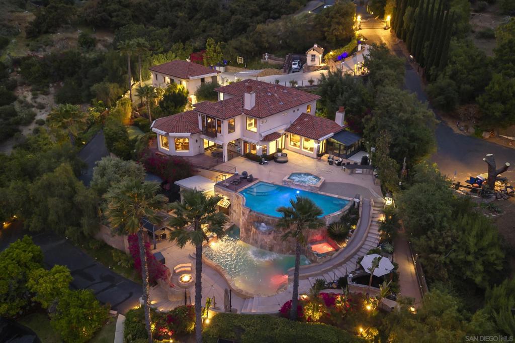 Welcome to Casa Del Lago. A lakeside escape like no other, tucked behind private gates on over 2.5 acres of beautifully manicured land. Framed by unobstructed views of Lake Hodges and the surrounding hills, this one-of-a-kind estate offers the ultimate blend of seclusion, comfort, and natural beauty. The main residence evokes the warmth of a Mediterranean escape, with timeless architectural details and a seamless connection to the outdoors. A junior suite on the main level offers flexibility and comfort for guests or multigenerational living. Every window invites nature in, with gentle breezes, golden light, and expansive views creating a sense of calm throughout the day. A separate guest house with its own garage provides total privacy for visitors or live-in support, while the surrounding grounds transform everyday living into something truly exceptional. Two pools joined by a cascading waterfall and winding slide serve as the centerpiece of an outdoor space designed for relaxation, play, and unforgettable gatherings. Thoughtfully designed with modern sustainability in mind, the estate includes a solar system, four Tesla Power Walls, and three EV charging stations. Multi-level fencing ensures peace of mind for pets and little ones, while the expansive grounds offer freedom to roam. Rarely does a property strike this balance: luxury without pretense, privacy without isolation, and beauty that feels both wild and intentional.