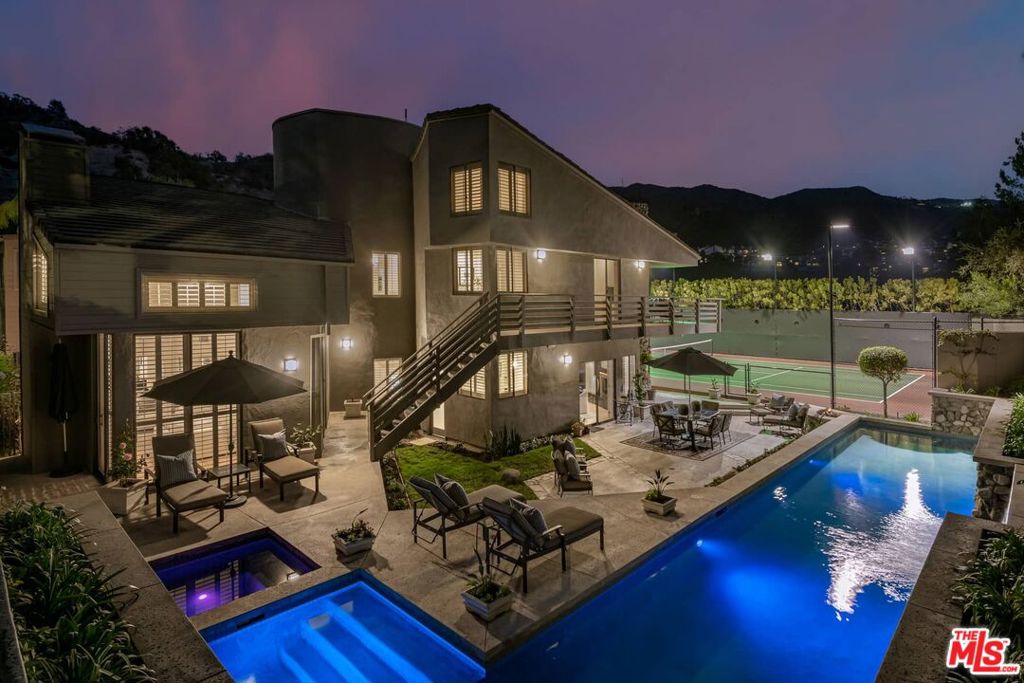 Never has it been more essential to find sanctuary in a secure, well-established community. Set on over half an acre behind the 24/7 guard gates of the Palisades Country Estates, this extraordinary 5-bedroom, 4.5-bathroom estate offers a rare combination of peace of mind, architectural brilliance, and an unrivaled indoor-outdoor lifestyle. One of the few properties in this exclusive enclave to boast a full-size tennis court, this nearly 5,500 sq ft residence is designed for those who value both active lifestyle and sophistication. The home's striking Steinbrueck+Dianella design begins at the atrium entry with tranquil water feature, guiding you into a space filled with curved walls, soaring ceilings, and a dramatic circular skylight that pours light into the heart of the home. Inside, elegant architectural niches offer a perfect stage for curated objet d'art, while the formal living room, with its soaring windows and refined fireplace, flows easily into a private office with its own exterior entrance. The family room exudes warmth with exposed wooden beams, a second fireplace, and a wet bar for effortless entertaining. A gourmet kitchen anchors the home, outfitted with top-tier appliances, custom cabinetry, a walk-in pantry, and direct access to the formal dining space. Upstairs, the primary suite is a restful retreat with a spa-like bathroom, fireplace, private coffee bar, walk-in closet, and balcony access for quiet morning reflections. The upper level also features a guest suite, three additional bedrooms, dedicated office space, and a laundry room. Property also features generous parking with 3-car garage. But what truly sets this property apart is its resilient lifestyle offering. Whether hosting under the stars, swimming laps in the pool and spa with waterfall, gathering by the fire pit, or playing on your private tennis court, this home invites you to thrive in a space designed for health, leisure, and security. Tucked away in a naturally protected area of the Palisades, yet just moments from Caruso Village, hiking trails, and the Pacific Ocean, this is more than a home, it's a post-fire refuge for those who seek architectural soul and everyday inspiration.