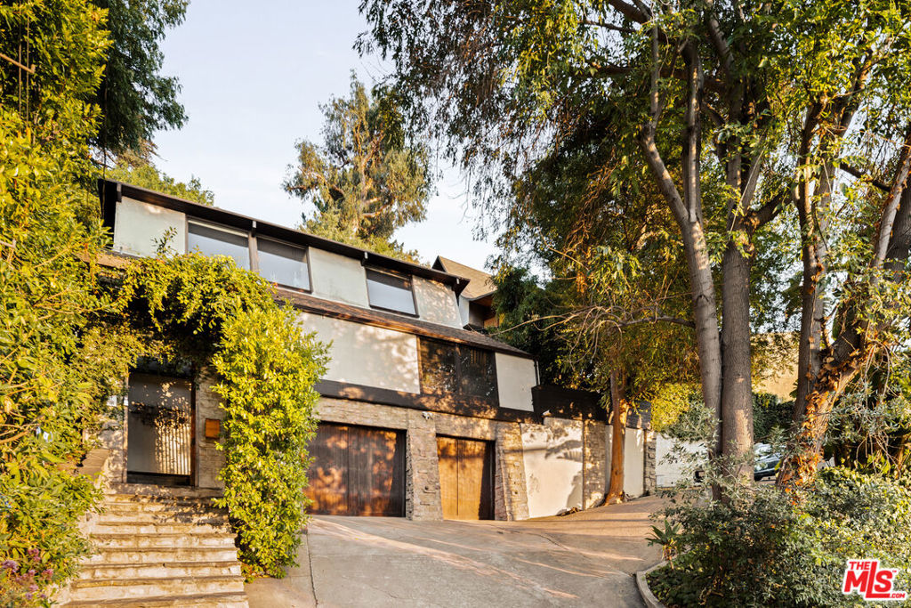 Tucked into Franklin Hills, this 1963 architectural gem by Stephen Alan Siskind is a rare expression of mid-century vision - dramatic, warm, and truly one of a kind. A soaring, asymmetrical gambrel ceiling defines the great room, where angular lines and floor-to-ceiling windows frame lush canyon views and fill the interiors with natural light. The result is a home that feels both expansive and intimate - like a modern treehouse in the city. The updated kitchen features stone countertops, custom cabinetry, and sleek appliances. With three bedrooms and two baths, the flexible layout includes a guest room on the main level and two upstairs bedrooms, including a tranquil primary retreat. Outside, multiple patios invite al fresco dining and cozy evenings by the built-in fireplace. The home's standout feature is a detached, glass-wrapped studio set among the trees - ideal as a home office, creative space, or guest suite. Just minutes from Los Feliz Village, Griffith Park, and top-rated schools, 3986 Clayton offers mid-century living at its finest: peaceful, architectural, and perfectly placed in the heart of the city.