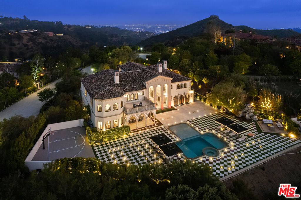 An enchanting property steeped in unrivaled elegance, 9 Beverly Ridge Terrace is utterly unparalleled in its design, scale and style. Custom-crafted by renowned designer Robert Rivani, the home fuses ultra-romantic details and modern conveniences with a divine Italianate aesthetic. Comprising seven all-ensuite bedrooms and nine baths, this three-level home spans 15,200 square feet on 1.7 acres of park-like grounds poised to host epic, large-scale gatherings and picture-perfect intimate soirees. Set behind the double-guarded gates of Beverly Ridge Estates, 9 Beverly Ridge immediately makes an indelible impression. Wind through a large motor court with a central fountain to arrive at the curved stone entry, which opens to reveal a foyer with triple-vaulted ceilings, walls of windows that frame incredible canyon views, crown-like chandeliers and medieval-inspired wall sconces. From here, a curved wrought-iron-railed staircase leads to the upper levels, while polished stone and hardwood floors beckon to grand main-level living spaces. Rooted in imaginative design, this home's distinct features and one-of-a-kind spaces delight at every turn. On the main level, a fantastical lounge with walls and ceiling covered with life-like faux flowers and a 300-piece chandelier resembling butterflies, creating a wonderland-like garden room. The gourmet kitchen boasts stone counters, an eat-in island and stainless steel Viking appliances. A bar room is replete with intricately carved coffered ceilings and a formal dining room is illuminated by the estate's signature crown-like chandeliers. Ascend to the second level's 2,000-square-foot primary retreat to find a bespoke wood fireplace, private terrace and spa-like bath with soaking tub and oversized steam shower. Set on a rare flat lot, one of the community's largest, the estate's exquisite backyard features jet-liner canyon and sunset views and a pool and spa surrounded by a lounge area with harlequin-patterned pavers laced with squares of grass and flowers. Thoughtful outdoor amenities also include a sports court and a covered patio. Additional estate features include a library, gym, a six-car subterranean garage and smart home technology. 9 Beverly Ridge Terrace is located mere minutes from the shops, and restaurants of downtown Beverly Hills, and sits within the coveted Beverly Hills Post Office district.