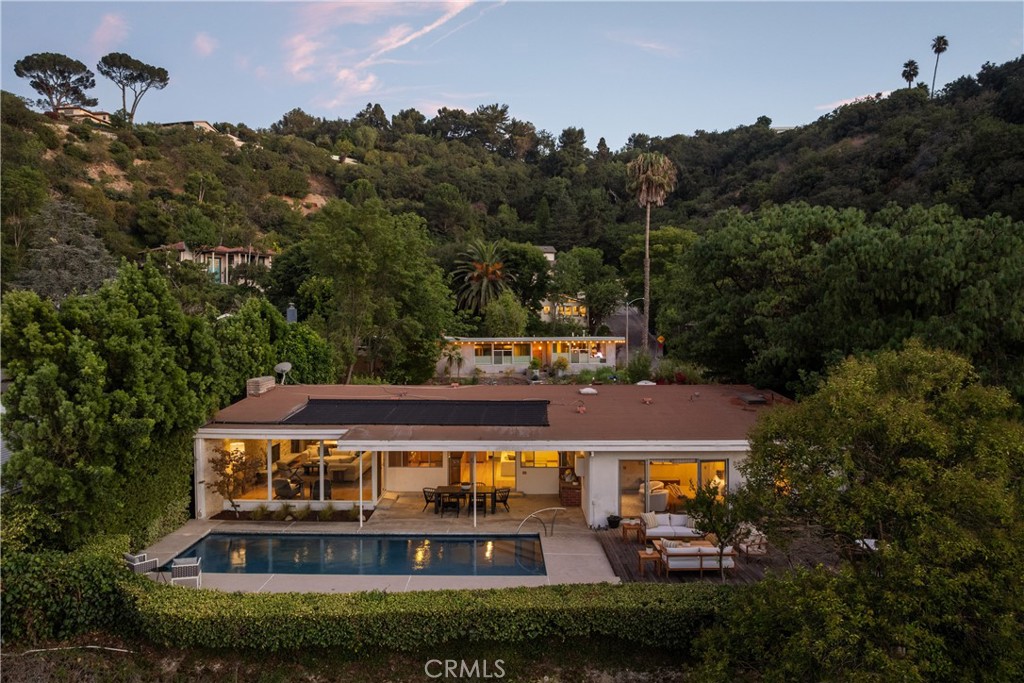 Mid-Century Modern one-story retreat located below Mulholland Drive in a breezy micro-climate with breathtaking mountain and city views. The functionality and beauty of this home is designed for easy living found in Vogue. This rare south of the Boulevard Sherman Oaks gem will delight and entertain you. Featuring 4 bedrooms plus a versatile bonus room, this home balances iconic architectural details with modern comfort. Authentic terrazzo floors welcome you into the vaulted-ceiling foyer, where clerestory windows and skylights fill the interiors with natural light. A dramatic indoor/outdoor limestone wall with a fireplace anchors the family and dining room, while wood-beamed ceilings and full-height walls of glass frame the dazzling vistas. The primary suite offers an adjacent working office, large walk-in closet and poured in place concrete spa-like bath. Three additional bedrooms and a flexible bonus room – ideal for a gym, office or playroom – provide space and privacy for every lifestyle. The kitchen retains its true Mid-Century character with solid wood cabinetry and connects to a second family room overlooking the views. An enviably large laundry room with lots of built-in cabinetry adds functionality and storage. Outside, the sparkling blue glass-tile pool (with a refreshing deep blue hue), an expansive deck and multiple lounging and dining areas create the perfect setting for entertaining or quiet evenings under the twinkling city lights. Tucked near the end of a peaceful cul-de-sac, yet just moments from Ventura Boulevard, this rare Mid-Century Modern gem combines style, function and location. Properties like this rarely become available.