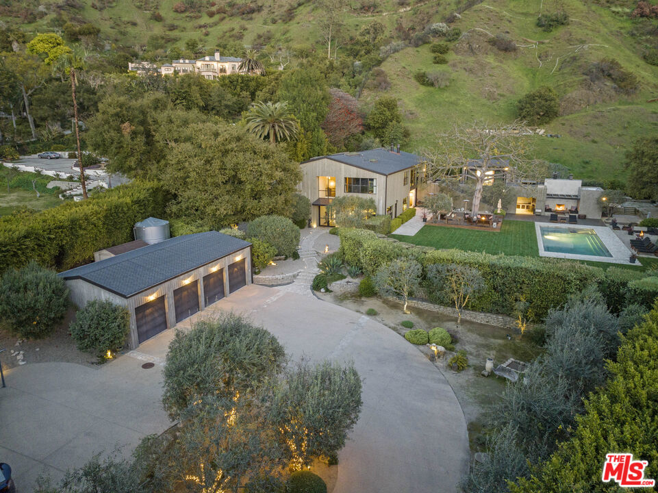 Magical and One-of-a-Kind Barn House in Serra Retreat designed by architect Michael Kovac and crafted by the world-renowned designer Vanessa Alexander, this exceptional property is a true entertainer's dream. It masterfully blends modern sophistication with the tranquil beauty of nature. Nestled within the inviting inclusive yet exclusive, guard-gated neighborhood of Serra Retreat, this home offers the perfect balance of privacy, luxury, and stunning natural surroundings, with expansive floor-to-ceiling windows and doors that allow natural light to pour in while offering breathtaking views of the surrounding mountains and lush gardens. The property features six spacious bedrooms and six bathrooms. The home is perfectly suited for indoor-outdoor living, with seamless flow between the interior and exterior spaces. The landscaping, fruit trees and raised garden beds are meticulously maintained by two dedicated professionals who tend to the property weekly, ensuring its beauty year-round. A charming pergola leads you to a private outdoor infrared sauna, offering the ultimate in relaxation and wellness. The home is also equipped with smart home technology, including Sonos speakers. Sustainability is at the forefront of this design, with a 5,000-gallon water reserve tank, a diesel generator for backup power, an instant hot water and filtration system, and a power transformer that enhances energy efficiency. The media room is equipped with Apple TV, making it the perfect spot for movie nights or relaxation, while the steam shower in the bathroom offers a luxurious touch for personal wellness. The outdoor space is just as impressive, featuring two expansive patios ideal for lounging, dining, and entertaining. The outdoor dining area comes complete with a fire pit, BBQ, pizza oven, perfect for enjoying cool evenings under the stars, and the pool and spa offer year-round enjoyment. For those with creative pursuits, a flex room serves as a versatile space, perfect as a recording studio or home office. The backyard, bathed in sunlight, provides ample space to enjoy nature, offering a peaceful retreat right at home. The location is unmatched, offering a rare microclimate with abundant sunshine and sweeping mountain views, while still being close to local hotspots like Blue Bottle Coffee, a favorite gathering place for Malibu locals. This is a place like no other, where you can unwind, create, and live in perfect balance.