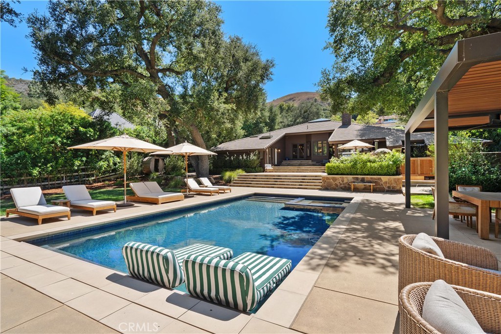 Inspired by Frank Lloyd Wright’s iconic design principles, this stunning architectural home is nestled within the prestigious guard-gated community of Bell Canyon in Ventura County. From the moment you arrive, the home’s striking curb appeal impresses with its extensive brickwork and meticulously maintained landscaping. Double glass doors open to a grand living room featuring a dramatic pyramid-shaped vaulted ceiling with skylight, a floor-to-ceiling slate fireplace, and a built-in aquarium—creating an unforgettable first impression. The kitchen is a chef’s dream, offering custom cabinetry, granite countertops, stainless steel appliances, a center island with prep sink, and rich hardwood flooring. The breakfast area overlooks vibrant rose bushes through an expansive wall-to-wall garden window with a retractable window covering. The primary suite is a serene retreat with a sitting area, vaulted ceilings and French doors that open to the backyard. The spa-like ensuite bath offers quartz countertops, dual sinks, ample enclosed closets, a luxurious clawfoot tub, and a generous walk-in shower. A secondary bathroom has granite countertops, Travertine floors, and a custom-tiled shower. Additional highlights include a warm and inviting den, currently used as a gym, with exposed brick & and skylights. Throughout the home, you'll find exquisite design elements such as tongue-and-groove solid wood walls and ceilings, stained glass windows, custom doors, newer carpet and paint plus unique architectural angles. Other recent upgrades worth mentioning are the newer tile roof, AC (3 units), garage with custom built-ins, epoxy floor and garage doors. A series of single-light French doors open to an expansive, reimagined resort like backyard—mostly flat and perfect for entertaining. with a pebble tech pool and spa a motorized pool cover a sauna, outside shower, and free-standing cold plunge for ultimate relaxation. The fully equipped outdoor kitchen features top-of-the-line appliances, including a pizza oven, paired with a covered dining pergola with an adjustable roof for effortless al fresco gatherings. All of this is set against the peaceful backdrop of Bell Creek flowing at the edge of the property. Bell Canyon residents enjoy access to amenities including an equestrian center, fitness center, tennis courts, scenic trails, and tranquil parks—all within the acclaimed Las Virgenes School District. This one-of-a-kind property must be experienced to be truly appreciated.