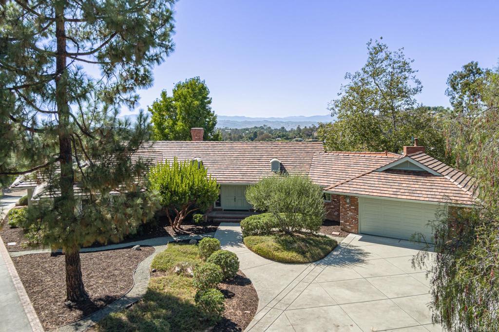 A tree-lined driveway welcomes you to this timeless single-story Fallbrook home, set on 4.42 acres with rolling slopes, mature trees, and sweeping westerly views. Built with quality craftsmanship and thoughtfully updated, this 3,182 sq ft residence blends character, comfort, and functionality with space to live, work, and entertain. The heart of the home is its inviting living areas, anchored by charming brick fireplace that brings warmth and timeless style. Expansive windows capture the beauty of the hills and mountains, filling the home with natural light and framing unforgettable sunsets. The cheerful breakfast nook, surrounded by windows, opens directly to one of several patios—perfect for morning coffee or relaxed outdoor dining. The gourmet kitchen is equipped with stainless steel appliances including a Sub-Zero refrigerator and Viking range, abundant counter space, and easy flow to the breakfast nook and dining areas, making it ideal for everyday living or entertaining. Featuring 3 bedrooms and 3 bathrooms (2 full, 1 half), all on the main level, the floor plan is practical and welcoming. The primary suite offers generous proportions and direct outdoor access, while guest bedrooms are comfortable and versatile. A spacious laundry area and walk-in pantry provide everyday convenience, reflecting the home’s well-planned design. Outdoors, the property offers endless possibilities. Multiple patios, mature landscaping, and a park-like grove with mature shade trees create serene spaces to enjoy the outdoors. There is room for a pool, additional fruit trees, or even a mini farm. Existing citrus trees enhance the country lifestyle.The grounds feel like a private park with mature shade trees, meandering paths, and multiple brick patios—a perfect canvas for a future pool, orchard expansion, or equestrian possibilities. The permitted 900+ sq ft detached workshop is fully equipped with 220 electrical and air conditioning, making it ideal for hobbies, projects, or vehicles, with possible ADU conversion potential (buyer to verify). Parking includes an attached 2-car garage plus plenty of room for RVs, a boat, or other toys. This home’s solid construction, brick details, fireplaces, recent updates, and gourmet kitchen capture the best of Fallbrook living. With single-level convenience, westerly views, and glowing sunsets, it offers both retreat and opportunity in a peaceful rural setting.