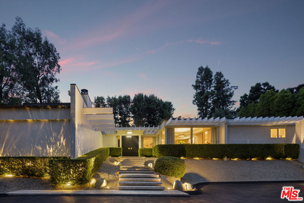 Situated on one of Encino's most sought-after streets, this gated Mid-Century Modern estate pairs architectural elegance with refined, contemporary interiors. A dramatic entry welcomes you into an open floor plan filled with natural light, designer finishes, and expansive glass walls that frame lush outdoor views. Sophisticated living and dining areas feature statement lighting, custom accents, and seamless flow ideal for entertaining. The sleek chef's kitchen includes premium appliances and built-in breakfast seating, while multiple lounge spaces offer comfort and style throughout. Outside, a private backyard oasis awaits with a sparkling pool, sun-soaked patios, and mature landscaping for total seclusion. This single-story stunner perfectly combines timeless design and modern luxury in one of the Valley's most coveted neighborhoods.