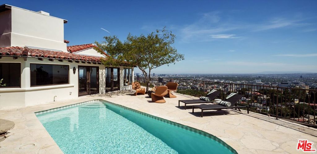 Perched atop a private promontory at the end of a quiet cul-de-sac in the esteemed Outpost Estates, 6911 Los Tilos is a custom-crafted Spanish Revival with a warm, rich, and inviting aesthetic completely reimagined from the ground up by LoBello Designs, styled in partnership with Olive Ateliers. With breathtaking, unobstructed views spanning from the Hollywood Sign to the Pacific Ocean, and everything in between, the home gives the distinct feeling of living above the city rather than within it. Upon arrival, guests are welcomed into an open-concept main floor, where a cozy sitting room features an original brick fireplace and mantle, adjacent to a charming breakfast nook and the show-stopping chef's kitchen. Anchored by a La Cornue range, the kitchen is appointed with custom oak cabinetry, Calacatta Rhino marble, Waterworks brass fixtures, and built-in Miele appliances. Completing the ground floor are a formal dining room, two guest bedrooms connected by a Jack-and-Jill bath, a powder room, and a delightful sunroom / den offering panoramic views, ever-changing light, and direct access to the expansive outdoor observation deck, pool, and bonus structure--perfect for a home office, gym or out of town guests. Upstairs, natural light pours in from all directions through expansive windows and skylights, reflecting beautifully off Meoded Concretta plaster walls. The primary suite is a true sanctuary which features a cinematic, one-of-a-kind view as well as a spacious en-suite closet and bath, with custom cabinetry, a large soaking tub and an Arto Brick & Tile shower. An additional upstairs guest bedroom mirrors the primary in style, offering custom finishes, an en-suite bath, and its own private balcony. With some of the best views LA has to offer, that include the Griffith Observatory, Downtown LA, the Hollywood Hills, and Catalina Island, 6911 Los Tilos offers unmatched privacy, architectural integrity, and inspired design in a coveted location.