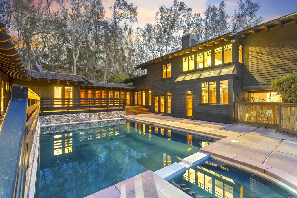 Tucked into the lush, forested enclave of Rancho Santa Fe’s prestigious West Covenant, this stunning contemporary Craftsman estate offers an extraordinary blend of inspiration, modern comfort, and unspoiled natural beauty. Designed by Andy Herbruck and inspired by Pasadena’s iconic Gamble House, the residence is a true architectural gem—warm, inviting, and masterfully integrated into its idyllic surroundings. Set on 3.17 ultra-private acres, the home is enveloped by mature trees and open sky. Over 2,000 square feet of redwood decks and balconies offer peaceful spaces to dine al fresco, relax with morning coffee, or simply listen to the rustle of leaves in the breeze. Here, life unfolds in harmony with nature. Step inside to nearly 6,600 square feet of craftsmanship and comfort with 8 bedrooms, 5.5 bathrooms, and 6,596 square feet of refined living space.. A dramatic floor-to-ceiling river rock fireplace, rich wood finishes, and bespoke built-ins anchor the main living spaces. The U-shaped layout naturally separates the west wing—home to the primary suite, a secondary bedroom, the kitchen, and living room—from the east wing, where additional bedrooms offer privacy and flexibility for family or guests. French doors open from most of the rooms, spilling sunlight and fresh air into the home while offering seamless flow to the outdoors. The resort-style grounds feature a sparkling saltwater pool and spa, an outdoor kitchen with built-in BBQ, and expansive entertainment patios shaded by towering trees. The chef’s kitchen shines with granite counters, glass-front cabinetry, and a center island cooktop framed by picture windows that overlook the trees and sprawling deck. The formal dining room and great room—with custom bar and space for a pool table—create the perfect backdrop for gatherings large or small. Upstairs, the private primary retreat is a sanctuary unto itself. With high, beamed ceilings, large windows, treetop views, an office, and a newly upgraded bathroom, the suite exudes calm and quiet luxury. Step directly from your bedroom onto the upper deck for sunrise reflections or stargazing under the canopy. Ideal for multigenerational living, the home’s layout ensures connection and comfort without compromising privacy. Residents enjoy access to top-rated Roger Rowe schools, miles of equestrian and hiking trails, and the timeless charm of the Rancho Santa Fe Village, just minutes away. Beaches, shops, and the freeway are close by—yet the peaceful stillness of nature remains uninterrupted. This is more than a home—it’s a lifestyle immersed in nature, privacy, and architectural elegance. Schedule your private tour today and experience the soulful tranquility this remarkable estate has to offer.