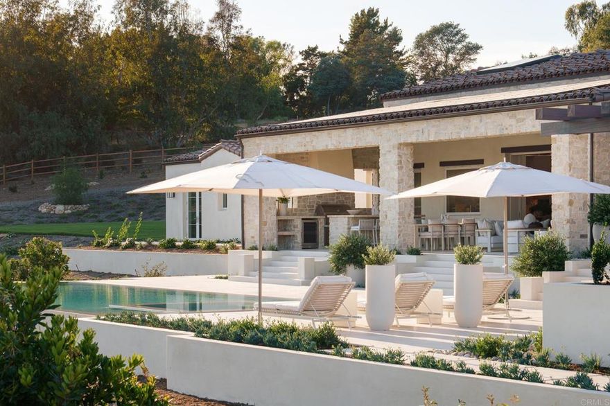 Completed in August 2025, this new build single-level estate represents the pinnacle of Covenant living. Privately gated and approached by an extended drive, the residence embodies timeless European elegance while embracing modern sophistication on 2.54 fully landscaped acres with an expansive rolling hill view corridor.   A showcase of craftsmanship and luxury, built by master builder, Josh Herbst of Herbst Construction, the interiors reveal a curated collection of finishes that embody the prestige of the Covenant and the sophisticated lifestyle synonymous with this community. Airy, light-filled spaces are layered with natural stone at every turn—from timeless limestone and hand-glazed tile to Italian marble counters with protective finish. Imported slabs complement these surfaces, carrying a sense of refinement and artistry throughout the home. Custom cabinetry, sculptural fireplaces, and boutique-style closets softly illuminated like a couture atelier further elevate the interiors, while designer lighting further enhances the elevated ambiance throughout. Expansive vanishing doors blur the boundaries between indoors and out, opening the great room effortlessly to the exterior living and dining spaces.  The primary suite stands as a lavish private retreat, inspired by the Montage Los Cabos. A generous bedroom opens to a private patio with serene views overlooking the pool and landscape beyond, while a dedicated sauna enhances the sense of wellness and indulgence. The spa-inspired bath features dual water closets, dual vanities, a separate dual-head walk-in shower, and a soaking tub—all designed to offer an atmosphere of serenity and refinement.  At the center of the home lies a kitchen worthy of its own showcase: a 60” Officine Gullo range hand-forged in Florence, Gaggenau refrigeration with glass-and-steel interiors, and custom metal-framed cabinetry that feels more gallery than kitchen. This is a space that celebrates not only cooking but the art of gathering—designed for those who demand nothing less than the best.  The superior lifestyle extends gracefully outdoors, where sculpted grounds feel like a private resort. A vanishing-edge saltwater pool merges with the horizon, while expansive terraces, curated outdoor furnishings, and layered plantings establish both serenity and grandeur. Direct trail access connects the property to the community beyond, making nature and recreation seamlessly part of daily living. From sunrise swims to moonlit soirées, every detail of the landscape is designed for beauty and ease. The detached guest house, offering two bedrooms, two baths, laundry, and a garage office suite, ensures guests experience the same level of refinement as the main residence.  This estate is more than the sum of its extraordinary finishes and pedigree; it is a rare opportunity to own a home that redefines luxury in Rancho Santa Fe. 17965 Via De Fortuna is not just one of the finest properties on the market today—it is the home against which all others will be measured.