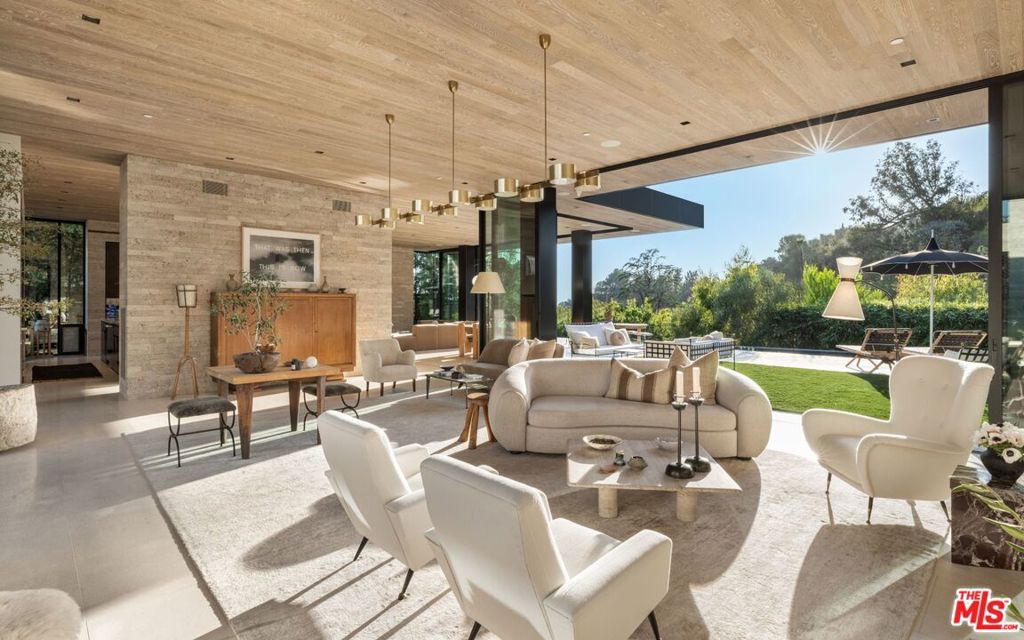 Discover world-class design and luxury in this organic contemporary Trousdale masterpiece crafted by award-winning architect Paul McClean and designer Lindsay Chambers and reimagined by Nate Berkus & Jeremiah Brent. Set on a prestigious, quiet cul-de-sac, this 11,000 SF home boasts an architectural exterior with custom Italian stonework. Mid-century-inspired steel grillwork surround the front door that opens to a showstopping glass bridge entrance. The two-story courtyard and walls of glass allow sunlight to fill the home and highlight the beautiful oak ceilings and Travertine walls. Glass walls open to a spectacular outdoor space featuring an expansive infinity pool with city and ocean views and a tranquil Japanese garden. The primary suite sits beside the pool as if it's floating above the water and offers a custom walk-in closet, and spa-like bathroom. Rejuvenate in the marble-clad indoor wellness center with hot and cold plunge, cedar sauna, and gym. Additional amenities include a stunning Nero Marquina-clad bar, home theater, subterranean auto gallery, and fairytale pink playroom. This architecturally significant home is a rare offering, even among the most discerning tastemakers in the city.