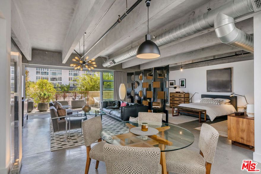 Experience true loft living in this one-of-a-kind residence at Element, a design-forward building featured in The New York Times and L.A. Architect Magazine for its distinctive concrete and steel construction, 11-foot ceilings, and exposed concrete beams. This industrial-style space is softened by designer finishes, offering a refined, creative living environment. This expansive, south-facing 1,540 SF unit features polished concrete floors, updated lighting, custom zebra wood cabinetry and closets, ripple fold drapery, and motorized light-filtering shades. Floor-to-ceiling aluminum-framed windows and Fleetwood sliding glass doors lead to a double-width private balcony, seamlessly blending indoor and outdoor living. The oversized 13' Carrara marble island with soft-close drawers, bar seating, built-in pantry, Viking Professional appliances, Brizo faucet, double-bowl sink, and wine fridge anchor the chef's kitchen, ideal for entertaining. The spa-like bath includes a double vanity, soaking tub, walk-in shower with dual shower heads, and custom linen cabinet. Note: This unit does not have enclosed bedrooms, offering a fully open floor plan perfect for creative customization. Additional Features: *Two parking spaces (tandem) with EV charger *Ample guest parking *Secure access, fitness center, bike storage *Community courtyard with fire pit and grill *Well-managed building with strong reserves. Located in the heart of the Marina Arts District with a Location Score of 92, just minutes from shops, restaurants, theaters, the beach, and marina. Don't miss this rare opportunity to live in one of the Westside's most architecturally distinctive and vibrant communities.