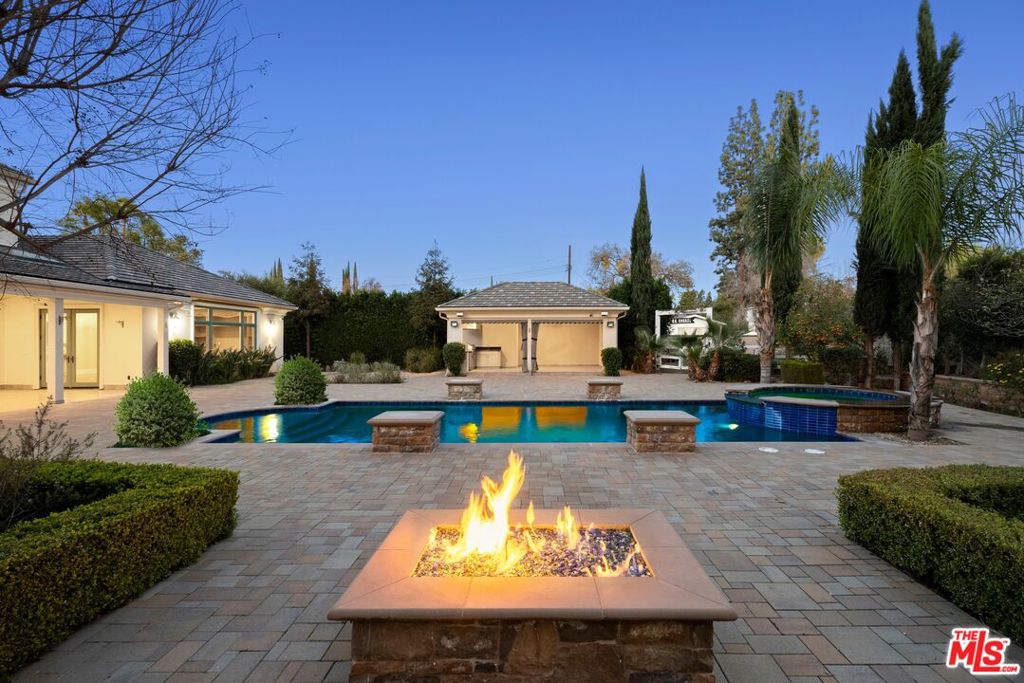 Featuring numerous entertaining spaces and recreational possibilities both inside and out, this gated cul-de-sac compound is positioned in a desirable, close-knit neighborhood where Woodland Hills meets Calabasas. Guests enter through a wrought-iron gate into the expansive motor court with mature trees, manicured landscaping, and courtyard. Inside, coffered ceilings overhead create a sense of richness and importance in the great room with traditional fireplace, formal dining, and a series of French doors opening to the outside. The large kitchen is appointed with an oversized center island, an abundance of cabinetry, garden window, and top-of-the-line appliances including Viking refrigerator and Wolf range with custom decorative hood and pot filler. The adjacent family room has a built-in media center with fireplace and breakfast nook. The primary suite, also with built-ins, includes French doors, plantation shutters, and a Venetian-inspired spa-like bathroom with dual sinks, separate tub, and large glass-enclosed shower. A walk-in wardrobe is fitted with custom shelving and dresser island. Secondary bedrooms and bathrooms are light-filled, and there is a bonus guest apartment on the second level, with its own separate entrance, kitchenette, en-suite bathroom, and patio. There is also a library/office, perfect for work or study. Outside, enjoy plenty of grass to roam and play, a fire pit for evening conversation, and a black-bottom pool and spa that centers the backyard spaces. There is even an outdoor living room and a separate pavilion which houses an outdoor kitchen with built-in barbecue and prep station. Nearby, a dedicated vegetable garden is great for growing organic produce. Welcome to this sought-after location near parks and schools, the 101 Freeway, The Commons at Calabasas, and Westfield Topanga shopping centers. Malibu beaches are also just a quick canyon drive away. Some photos are virtually staged.