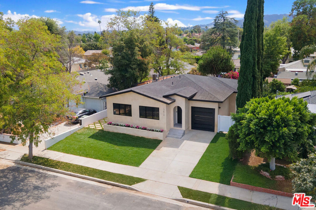 Welcome to this completely rebuilt family home in the heart of Encino. As you enter through the striking iron front door, soaring 10-foot high ceilings guide you into a light-filled, open concept kitchen and living space. The heart of the home, the kitchen features custom cabinetry, high end appliances, and a walk-in pantry. Details make all the difference; the spacious kitchen island has a gorgeous waterfall quartz countertop, and this same stunning material extends as the backsplash beneath the cabinetry. Adjacent to the kitchen, the living room centers around a sleek, electric fireplace and connects effortlessly to the backyard through a sliding glass door. A hallway off the entry leads to two guest bedrooms, each complete with an ensuite bath and custom built-ins, as well as a well-appointed laundry room, offering ample storage and a sink. All interior doors throughout the home are white oak, complementing the white oak floors. At the end of the hall sits the primary retreat, brimming with natural light and views of the luscious exterior, not to mention its custom walk-in closet. The primary bath provides dual sinks and an oversized shower with bench seating and dual shower heads. Aluminum sliding glass doors in both the primary and living room lead to the newly finished backyard, complete with a built-in barbecue. The yard is fully fenced and gated on either end, with lattice concrete pavers lining the home with thoughtful, functional hardscape. A single garage with a custom garage door provides a private entrance, opening directly into the living room and kitchen. After being taken down to the studs, expanded, and reimagined, this home is entirely brand new, including its HVAC, electrical, and plumbing. Embrace luxury and enjoy all Encino has to offer in this stunning space, conveniently situated near premier retail and dining options, as well as local parks and wellness offerings.