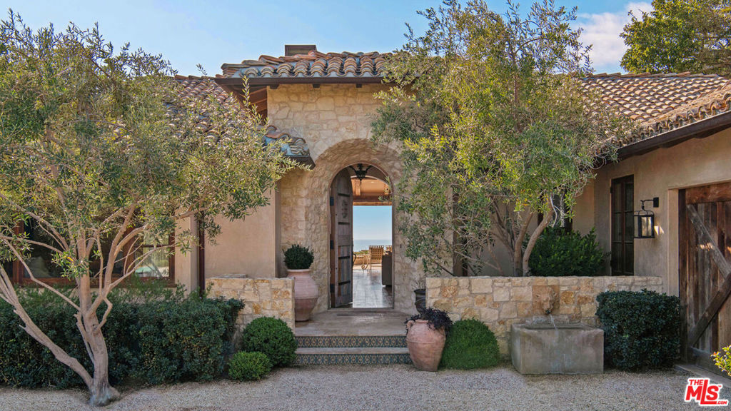 Discover unparalleled luxury in this exquisite French Country-style estate, a masterpiece of European elegance crafted by renowned builder Paul Brant Williger. Nestled in a prestigious enclave, this architectural gem blends breathtaking ocean views with world-class amenities and impeccable craftsmanship.A stone-arched entryway invites you into a world of sophistication, where soaring vaulted ceilings, reclaimed French oak floors, and antique wood beams create an ambiance of timeless grandeur. The living room, anchored by an antique wood-burning fireplace imported from France, seamlessly connects to the outdoors, offering an airy and inviting retreat. Adjacent, the great room charms with a cozy firewood nook, perfect for intimate evenings.The chef's kitchen is a culinary masterpiece, featuring a sprawling quartzite island, Caesarstone counters, and premium appliances, including a 6-burner Wolf range, dual Miele dishwashers, Sub-Zero refrigeration, a built-in Wolf microwave, and a Miele coffee machine. Custom antique French tiles, a built-in bar with wine storage, and vaulted ceilings elevate its allure. The formal dining room captivates with a fireplace, wood-beamed vaulted ceilings, and sweeping coastline vistas. A nearby powder room impresses with French tile floors, a floating sink imported from France, and bespoke lighting.The primary suite is a serene haven, offering ocean and pool views, a fireplace, and sliding doors to the lush backyard. Its spa-inspired ensuite boasts mosaic tile floors, stone counters, a double vanity, a walk-in shower with a marble bench, and an in-ground soaking tub framed by elegant French windows. Additional bedrooms feature vaulted ceilings, walk-in closets, and luxurious baths adorned with imported tiles and custom finishes.A converted garage serves as a versatile office or gym, complete with built-ins, skylights, and French doors opening to the garden. The well-appointed laundry room adds convenience with built-in storage, a new washer and dryer, and a wine fridge.The backyard is a private paradise, showcasing panoramic ocean views, a rectangular pool with an integrated hot tub, a fire pit with a custom-built couch, and a tranquil waterfall. A covered outdoor dining area, equipped with infrared heaters and an exterior fireplace, ensures year-round enjoyment. Hand-finished French limestone paves the yard, offering a slip-resistant, elegant surface.Uncompromising craftsmanship defines this estate, from imported antique doors to a handmade Tuscan tile roof. Modern conveniences include ultra-sound-resistant glass windows and sliders, push-button automatic shades, a whole-home generator, three-zone climate control, and a comprehensive security system. With four fireplaces, four fountains, and mesmerizing sunsets over Little Dume, this home offers an unrivaled living experience.Featured in Luxe Magazine and two HBO productions, this residence will soon be part of a gated, fire-wise community with low HOA dues. Every detailfrom antique French tiles to Excalibur hand-finished plaster wallsreflects the essence of a timeless European retreat, blending elegance, refinement, and extraordinary beauty.
