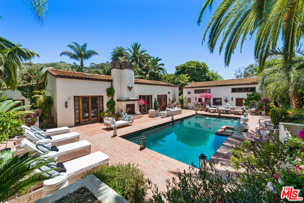 A tropical sanctuary compound in guard-gated Serra Retreat on nearly an acre of manicured grounds includes a 3-bedroom main house, 2-guest suites, large pool/spa brick terrace, tennis court w/pavilion, & 2-solariums used as a gym & yoga studio. The single-story main house features a large formal living room w/wood-truss ceilings, imported stone FP, & French doors on 3-sides for indoor-outdoor entertaining. The gourmet kitchen has a wood-block island, dining area, & French doors to pool terrace. A cozy family/media room w/French doors to patio. The owners retreat offers a sitting area w/stone FP, French doors to patio, dual closets, & tub/shower bath. The pool/spa terrace features a FP & BBQ island, & multiple sitting/dining areas. The 2-guest suites include a sitting room, bath, & loft-style sleeping room w/pool views. Numerous flagstone pathways meander past, lush lawns & mature trees, storybook sitting areas, a koi pond, & beautiful gardens. There is a 2-car garage, & guest parking.