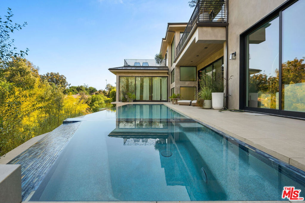 Warm modern Pacific Palisades home with pool and views! This impeccable newer build offers the height of luxury and refinement, complemented with warm, organic modern design and finishes throughout. Upon entry, explosive vistas of trees welcome from the formal living room and balcony, and a wet bar, powder room, office, and 3 en-suite bedrooms complete the top floor. Take the elevator or stairs down to the main level, where a jaw-dropping dining room flows into 2 distinct living spaces and a chef-worthy minimalist high-tech kitchen, all opening to an atrium garden on one side and infinity pool on the other side. Beyond the pool and spa, the outdoor area offers a firepit and built-in BBQ area. The entertaining and fun continue on the lower level, which offers a huge game room/lounge, complete with built-in bar, plus a powder room, and 1 en-suite bedroom. Nestled on a quiet street, just a couple blocks from Palisades Village, close to schools, Palisades Recreation Center, Potrero Canyon park and the beach! With all the modern amenities plus a chic modern design, surrounded by lovely treetop vistas, the property has the feel of a secluded luxury retreat but a location that offers the best of life in the Pacific Palisades.