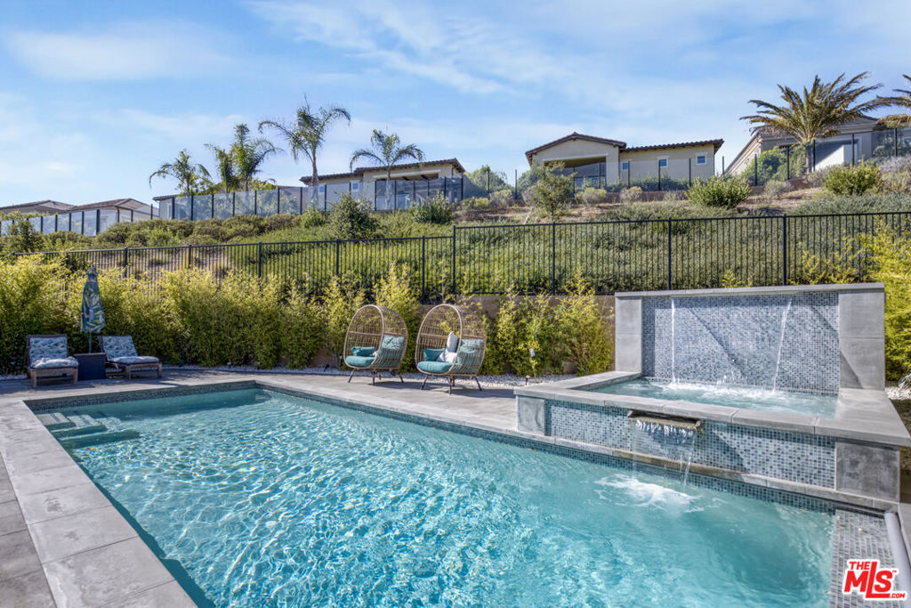 Experience elevated luxury in this exquisite 6-bedroom, 6-bathroom estate located in the highly sought-after Beacon Collection in Hillcrest at Porter Ranch, one of the premier gated communities in the Porter Ranch Hills. Built in 2019 and offering over 4,278 sq ft of meticulously designed living space, this newer construction home effortlessly combines timeless elegance with modern functionality. From the moment you step inside, you're greeted by soaring ceilings, elegant contemporary architecture, a dramatic curved staircase, and an open, light-filled layout ideal for both grand entertaining and everyday comfort. The heart of the home is the expansive gourmet kitchen, appointed with quartz countertops, rich brown cabinetry, stainless steel appliances, an oversized center island, gas range, and double ovens perfect for hosting dinner parties or casual family meals. The layout includes a spacious office/den/play room, ideal for working from home or creating a private retreat. The main level also features two large downstairs bedrooms, each with en suite baths, offering a rare and thoughtful option for multigenerational living, extended guests, or live-in arrangements. Upstairs, unwind in the spectacular primary suite, a true sanctuary featuring a private retreat area, an expansive walk-in closet, and a spa-like en suite bath with dual vanities, soaking tub, and a separate glass-enclosed shower. Four additional upstairs bedrooms provide ample space for family or guests, while a generous loft adds flexible living space perfect for a playroom, media lounge, or teen hangout. A full-size upstairs laundry room with storage cabinetry adds convenience to daily routines. Step outside and escape to your resort-style backyard oasis, where relaxation and entertaining seamlessly blend. Enjoy the custom pool, spa-ready pad, sleek fire pit lounge, and multiple outdoor seating areas all surrounded by professionally designed landscaping and privacy. Whether you're hosting summer gatherings or enjoying quiet evenings under the stars, this backyard is an entertainer's dream.Additional highlights include solar, a 2-car garage equipped with ceiling-mounted storage racks for optimal organization and dual-zone HVAC. Located near award-winning schools, top-tier shopping and dining at The Vineyards at Porter Ranch, scenic hiking trails, community parks, and easy access to the 118 freeway, this home offers the best of luxury living with suburban convenience. Rarely does a home combine such thoughtful design, spaciousness, and location this is your chance to live beautifully in one of Porter Ranch's most desirable enclaves.
