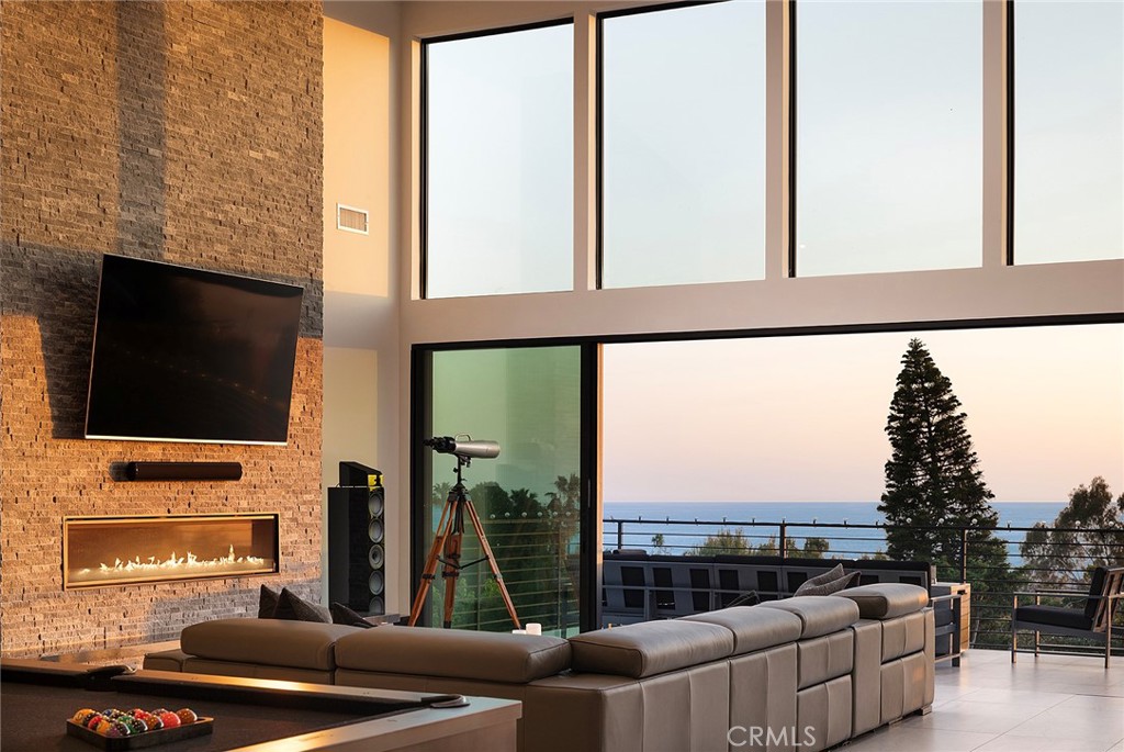 Completed in 2021, this architecturally significant residence in one of San Clemente’s most coveted hillside enclaves captures the essence of contemporary coastal life. Designed by noted architect Robert A. Hall, the home is a symphony of scale, light, and craftsmanship—each space unfolding with intention, intimacy, and awe. Set on a prime 16,777-square-foot cul-de-sac lot, its elevated position commands sweeping vistas of the Pacific Ocean, Catalina Island, fiery sunsets, snow-dusted peaks, city lights, and fireworks above the San Clemente Pier. Behind a custom African mahogany door, the approximately 4,849-square-foot interior opens with a soaring double-height foyer and unfolds into a gallery-like great room with 17-foot ceilings, a 76-inch linear fireplace, 20' x 8' foldaway glass doors, a 250-gallon saltwater aquarium, and a walk-in wet bar—blurring the line between indoor and ocean-facing outdoor living. The formal dining area glows with custom LED lighting and flows into a designer kitchen featuring Monogram appliances, sleek white cabinetry, solid stone countertops, a butler’s pantry with wine fridge, oversized island, and a fold-away pass-thru window to the terrace. Five ensuite bedrooms—including a guest casita and two suites with ocean-view balconies—offer refined retreats, while floating stairs framed in glass with wave-pattern railings lead to a stunning primary suite with a private view terrace, linear fireplace, and spa-inspired bath with jetted tub, skylit oversized shower, and boutique-style walk-in closet. Amenities include a dumbwaiter, Savant whole-house AV system, PEX plumbing, central vacuum, water softening and filtration systems, and a standing-seam metal roof. The freshly painted exterior, tropical landscaping with curated lighting, gated front yard, and private backyard offer a beautiful canvas for a future pool, spa, or ADU. This is more than a residence—it is a rare convergence of design, location, and lifestyle, crafted for those who see home as both refuge and revelation.