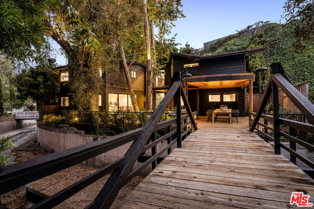 Tucked away in the idyllic enclave of Santa Monica Canyon, 327 E Rustic Rd is a 3-bedroom, 3.5-bathroom retreat with 2,834 square feet of thoughtfully curated living space. Extensively and tastefully renovated, the home was reimagined over the years in collaboration with Amber Interiors and architect Scott Prentice to blend organic elegance with elevated functionality. A 2022 renovation achieved a near-complete reconfiguration of the lower level and an expansion of the home's footprint. The result is a refined and inviting interior anchored by an open chef's kitchen featuring marble countertops, white oak flooring, custom cabinetry and top-of-the-line Wolf and Sub-Zero appliances. Oversized windows throughout bring in soft natural light and frame views of the canyon's surrounding beauty. Upstairs, two secondary bedrooms with en suite baths sit down a hallway from the serene primary suite, which features a spa-like marble clad bath with soaking tub, walk-in shower, dual vanities, hand painted terracotta floor tile, and a generous walk-in closet. A flexible open den once served as a fourth bedroom. Accessed by a private bridge and nestled alongside a creek, the property is surrounded by mature sycamores and soaring eucalyptus trees, offering both privacy and a deep connection to nature with easy indoor-outdoor living. An extensive landscape redesign added a flat grassy backyard, ideal for play, entertaining, or quiet reflection. Just moments from the beach, local restaurants, Canyon Square, and within the coveted Canyon Elementary School district, this one of a kind property pairs privacy, design pedigree, and location in one of LA's most treasured communities.