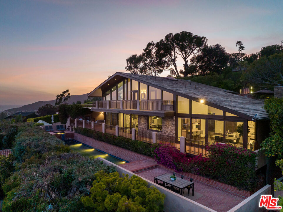 This magnificent 6 bed 7 bath located in Pacific Palisades was conceived by visionary architect, Ray Kappe. Remodeled in the early 2000's, the property overlooks the grounds of Lake Shrine and presents sweeping panoramic views extending from DTLA to Catalina Island, the Queen's Necklace to the beaches of Malibu. Located just moments away from both hiking and biking trails, the property grants access to all that Pacific Palisades has to offer. The home is outfitted with an Enphase Solar Energy system with a 4-battery array backup power supply, essentially making the property independent from the grid, and allowing for up to 3 days of backup power supply. The property also has a lower parking area, measuring approximately 50' x 75'. The home will be delivered with current plans and pending permits for a 7-car subterranean garage to be built, creating a deck area above with a 500 square foot game room. Sporting a fully equipped cook's kitchen with an open floor plan connecting to the formal dining room. Floor to ceiling window panels lend perfect perspective to take in the views. There are multiple family rooms, a media/screening room, an exercise room/studio with en suite bathroom, maid's quarters with a private bathroom, and a wine cellar with tasting area. On the exterior, there is a separate 3-car covered garage. In addition to the hardwood flooring and stone tiling throughout, this home is accented with stunning Mahogany wood-trim finish and custom glass lighting fixtures. The spacious deck outside overlooks the Pacific and provides access to the lap pool and spa below creating a breathtaking atmosphere and, facilitating both private lounging in the sun and hosting sunset entertainment. The two primary suites, each offering spectacular views of the ocean and the other three suites are all fitted with private en-suite bathrooms. In addition, located just below the pool area there is a separate guest house that is furnished with its own kitchenette and bathroom. This Zen-like retreat is a prime location for both long-term and short-term guests alike to make this estate their own personal oasis. Come claim your own private escape in this dream home that gives you an unparalleled views of the coastline and Pacific Ocean.