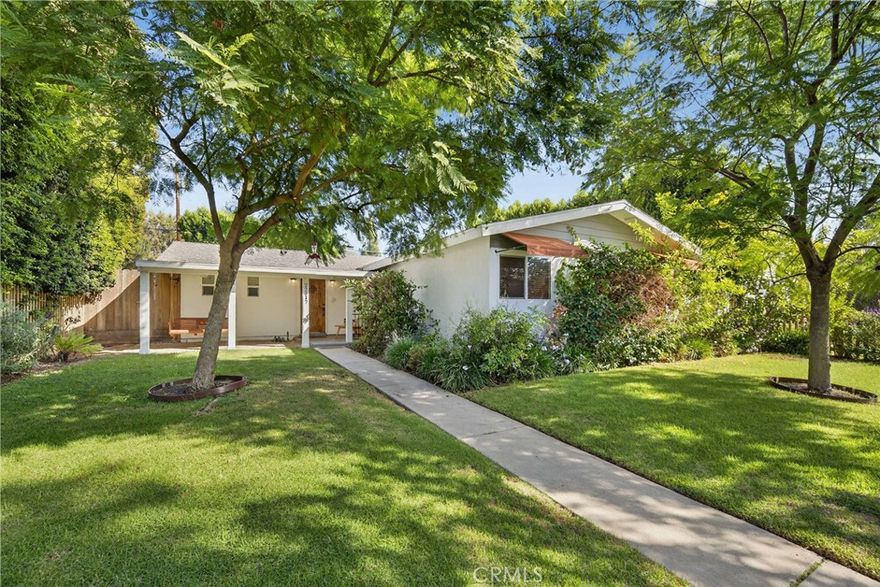 Tucked within a quiet West Hills neighborhood, this picture-perfect West Hills home blends midcentury appeal with modern sophistication. Framed by a classic picket fence, mature trees, and lush landscaping, the home’s inviting curb appeal leads to a covered front porch and an open, sun-filled floorplan designed for comfort and connection. Inside, wide-plank wood flooring flows through the main living spaces, complemented by recessed lighting and dual-pane windows and doors that enhance natural light throughout. The spacious living room centers around a sleek, floor-to-ceiling tiled fireplace, lending a warm, contemporary touch. The spacious kitchen delights with white cabinetry, quartz countertops, stainless-steel appliances, a farmhouse sink, and a modern glass tile backsplash—all part of the seamless great room for effortless entertaining. Sliding glass doors reveal a private backyard oasis featuring an inviting pool surrounded by a wraparound concrete patio, a covered porch area perfect for shaded lounging or outdoor dining, and a low-maintenance faux grass lawn. The primary suite offers serene pool views through a second sliding glass door that also offers direct backyard access, and a beautifully appointed full en-suite bathroom with a dual-sink vanity. Three additional bedrooms share a stylish full hall bath with modern finishes. A two-car garage accessed from the rear alley provides added convenience. Conveniently located near top-rated local parks, shopping, and dining destinations at Fallbrook Center and The Village at Topanga, with easy access to major thoroughfares including Topanga Canyon Blvd and Sherman Way.