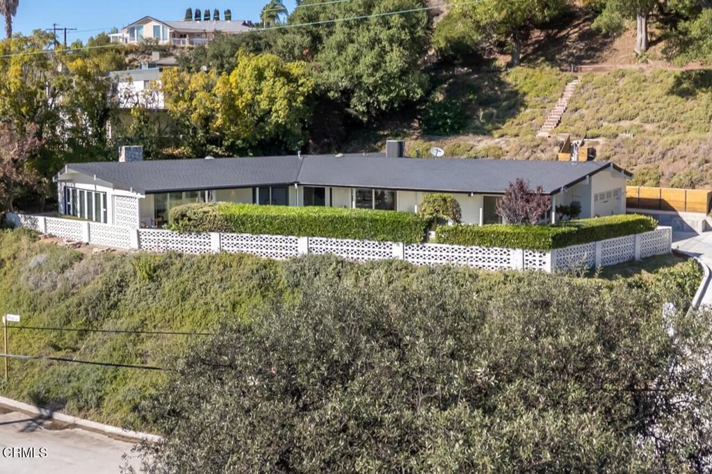 Perched atop a gentle hill in the sought-after San Rafael Estates, this exceptional mid-century modern home blends timeless design with modern comfort to elevate everyday living. A flat, private front yard framed by lush greenery creates a serene escape from city life and a welcoming first impression. Classic double doors open to a formal entry that sets the tone for the home's warm and inviting style. The spacious living room is bathed in natural light, anchored by a floor-to-ceiling stone fireplace, soaring beamed ceilings, and an expansive wall of windows that bring the outdoors in, the quintessential mid-century touch. At the heart of the home, the open-concept kitchen and dining area are designed for both daily living and effortless entertaining. The sleek white kitchen features an island cooktop, allowing the chef to stay connected while preparing meals, with views of the front yard. A designer chandelier, built-in shelving, and direct patio access make the dining area an ideal gathering space. The primary BR suite is a peaceful retreat, offering a private entry, a wall of closets, and a beautifully updated bath with dual vanities, illuminated mirrors, and a separate tub and shower. Two additional spacious, bright and airy bedrooms share a hallway bath. The back has a patio area and hillside stairs that lead to an upper terrace with sweeping views of the city and beyond offering a blank canvas for your outdoor vision, whether it's a garden, seating area, or entertaining space. Additional features include: an oversized two-car garage with direct interior access and newly finished epoxy floors, Central AC & Heat, wood engineered flooring & exposed beamed ceilings throughout, stainless steel appliances, and so much more. Located just minutes from the 2, 134, 5 & 210 freeways and a short drive to DTLA, it's the perfect combination of convenience and tranquil escape.