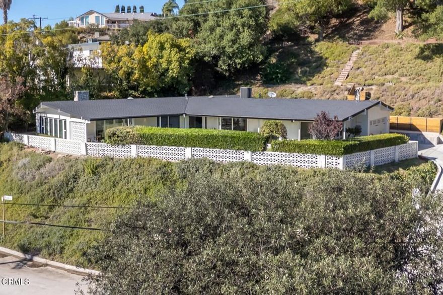 Perched atop a gentle hill in the sought-after San Rafael Estates, this exceptional mid-century modern home blends timeless design with modern comfort to elevate everyday living. A flat, private front yard framed by lush greenery creates a serene escape from city life and a welcoming first impression. Classic double doors open to a formal entry that sets the tone for the home's warm and inviting style. The spacious living room is bathed in natural light, anchored by a floor-to-ceiling stone fireplace, soaring beamed ceilings, and an expansive wall of windows that bring the outdoors in, the quintessential mid-century touch. At the heart of the home, the open-concept kitchen and dining area are designed for both daily living and effortless entertaining. The sleek white kitchen features an island cooktop, allowing the chef to stay connected while preparing meals, with views of the front yard. A designer chandelier, built-in shelving, and direct patio access make the dining area an ideal gathering space. The primary BR suite is a peaceful retreat, offering a private entry, a wall of closets, and a beautifully updated bath with dual vanities, illuminated mirrors, and a separate tub and shower. Two additional spacious, bright and airy bedrooms share a hallway bath. The back has a patio area and hillside stairs that lead to an upper terrace with sweeping views of the city and beyond offering a blank canvas for your outdoor vision, whether it's a garden, seating area, or entertaining space. Additional features include: an oversized two-car garage with direct interior access and newly finished epoxy floors, Central AC & Heat, wood engineered flooring & exposed beamed ceilings throughout, stainless steel appliances, and so much more. Located just minutes from the 2, 134, 5 & 210 freeways and a short drive to DTLA, it's the perfect combination of convenience and tranquil escape.