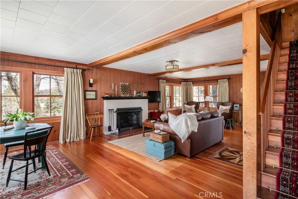 A Timeless Mountain Retreat in Lake Arrowhead’s Coveted Palisades Neighborhood
Perched at the crest of Lake Arrowhead’s desirable Palisades community, this charming 1949 cabin is a rare blend of vintage character and modern comfort. Thoughtfully preserved and beautifully updated, it sits among soaring oak and pine trees—offering a tranquil retreat that perfectly captures the spirit of mountain living. Quintessential charm abounds in the beamed main living area, where perfectly placed Anderson wood windows bathe the space in natural light. Impeccably restored Douglas fir floors and rich combed mahogany paneling exude warmth and craftsmanship, complemented by tasteful slate accents in the kitchen and baths. The expansive first level features airy, connected living spaces that flow effortlessly to the serene outdoors. A sophisticated dining room with custom built-in cabinetry opens to an oversized, elevated deck—ideal for entertaining or quiet relaxation amid mature natural foliage. A lush front garden, complete with roses, apple trees, and seasonal blooms, creates another inviting setting for year-round enjoyment.
The well-appointed kitchen retains its vintage charm while offering modern updates and convenience. A full bath and additional storage complete the main floor. Upstairs, three character-filled bedrooms offer dappled light and tranquil treetop or filtered lake views. A stylish second bath with vintage-inspired details and an enclosed laundry area complete the upper level. Blending history, craftsmanship, and comfort, this classic Lake Arrowhead residence offers a timeless retreat in one of the mountain’s most sought-after neighborhoods. Central A/C, upgraded systems and ample flat parking complete this one of a kind offering. Adjacent vacant land and 1/2 double dock available for extra.