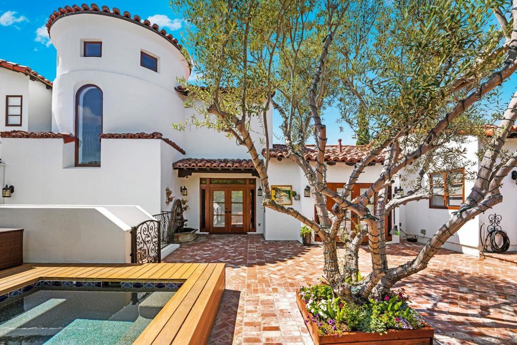 Welcome to Villa Conde, a 1931 Spanish Colonial Revival residence set on a private cul-de-sac in North Mission Hills. This home blends historic architecture with carefully considered modern design. Rooted in the heritage of one of San Diego’s most architecturally rich neighborhoods, it showcases original gumwood built-ins, beamed ceilings, hardwood floors, Venetian plaster walls, and mahogany windows. A signature Santa Barbara-style turret tower adds character and anchors the home’s striking curb appeal. Formal living and dining rooms offer elegant entertaining spaces, while the chef’s kitchen features Wolf and Sub-Zero appliances, travertine counters and a sunny breakfast nook with access to the courtyard. The bonus room, an extension of the family room, is ideal for a game room or play area. Upstairs, the primary suite features a custom walk-in closet and a peaceful sitting room with ocean and bay views. An additional upstairs room with built-in closets makes a perfect nursery or study. On the main level you will find two large rooms ideal for intergenerational living. One bedroom features an ensuite bath and is complemented by a light-filled bonus space, perfect for a home gym or studio. The front of the home, framed by palm trees, strawberry trees, and a curated herb garden create a lush, inviting entry. Along the side, a dedicated dog run caters to four-legged companions, an ideal touch for pet lovers who don’t want to compromise on design. A tranquil retreat awaits centered around a 100-year-old imported olive tree in the backyard. A plunge pool, fountain, and a bui