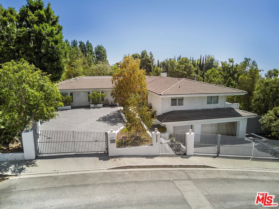 This elegant, single-level contemporary home, located minutes from Rodeo Drive, is gated and set back from the street, offering both privacy and security. The open floor plan effortlessly merges the living, dining, and family areas, creating a perfect space for both entertainment and quiet relaxation. A separate office area adds functionality to the layout. Walls of glass open to a serene outdoor oasis, featuring a sparkling pool, spa, and picturesque views, seamlessly blending indoor and outdoor living. The chef's kitchen is equipped with state-of-the-art stainless-steel appliances and features a large center island, creating an ideal space for cooking and gathering. The primary suite offers a private retreat with its own office area, and a spacious spa-style bathroom complete with double sinks, a vanity, and a steam shower. The lower level features a gym and a three-car garage, while the gated driveway offers ample additional parking.