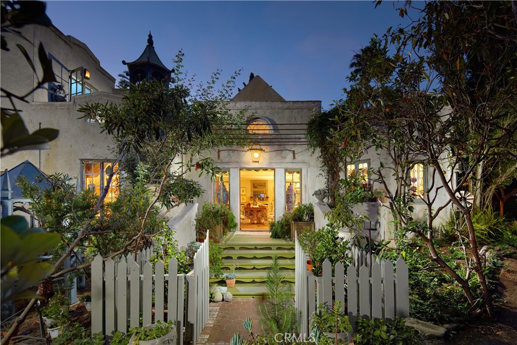 Two separate single-family homes set across three lots totaling nearly one-half acre, this historic Doheny estate surrounded by century-old trees invites you into a world where time slows and every corner whispers a story. The estate embodies a passion for authenticity, artistry, and romance — shaped most notably by antique dealer Gephard Durenberger, whose eye for European craftsmanship defined its timeless character and layered soul, and refined by interior designer Eric Guenther, whose stewardship has preserved its architectural integrity. The story begins with the original summer house built in 1925 and measuring appx 1,799 square feet, which was envisioned as the first in a planned enclave of retreat homes by Ned Doheny — predating the iconic Doheny House by three years. Intimate in scale yet rich in character, the 2-bedroom, 2-bathroom summer house evokes a rustic European sensibility, enhanced by hand-troweled plaster walls embedded with straw, marbleized painted finishes, and antique windows and doors that allow the home to appear as if it could date from 1725–1925. Decades later, the main house was thoughtfully added with equal reverence for the past, yet intentionally distinct—set apart by its separate street access. The two-bedroom, two-bath residence draws from European architectural traditions and features a cruciform layout anchored by a 24-foot-high folly that invites natural light to cascade through antique windows. Period details enrich every corner — from a 15th-century entry door and reclaimed 19th-century pine floors to antique French tiles — all contributing to the home’s timeless atmosphere and authenticity. The gardens, crafted by Florence Yoch — the renowned landscape designer behind Tara’s iconic grounds in Gone with the Wind — unfold as intimate “rooms,” originally conceived as nine distinct garden spaces framed by mature trees and hedges. Every view was carefully considered, preserving sightlines that connect house and garden as one harmonious whole. A Gothic aviary, French spire-turned-fountain, tea house, private pool, al fresco dining vignettes, and rose bushes gifted by the Duchess of Windsor enrich this poetic landscape. A rare opportunity to own a property that has welcomed designers, dignitaries, and tastemakers, yet remains deeply personal — a place where history, artistry, and the beauty of a life well-lived come together. Here, history is not just preserved; it is felt.