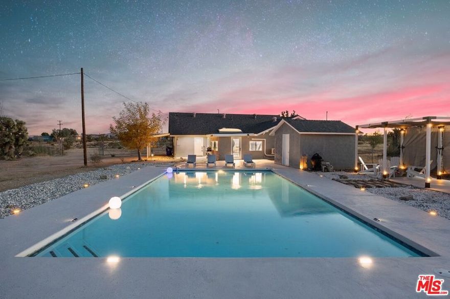 Generating $80,000 in annual gross income, this fully furnished, turnkey 5-bedroom, retreat delivers exceptional short-term rental performance and high-desert luxury. Set on five private acres in Yucca Mesa, the 2,040 sq ft home has been fully remodeled with designer finishes, including luxury vinyl plank flooring, recessed lighting, and a modern kitchen with a new cooktop, Samsung Bespoke refrigerator, shaker cabinetry, and butler's pantry. The open-concept layout is bright and spacious, ideal for entertaining. The primary suite features a spa-inspired en-suite bath, while a fifth bedroom in the pool house offers a private entrance for guests or rental flexibility. Outdoors, enjoy a resort-style setting with an Olympic-sized pool, hot tub, firepit, hammocks, and a custom Linx patio cover, all surrounded by sweeping desert and mountain views. Additional features include RV hookups, 220V carport, a storage unit, and a custom enclosed area suitable for events or parking. With HV/RL zoning, and room to expand, this property offers both immediate cash flow and long-term growth potential just minutes from Joshua Tree National Park and Pioneertown.