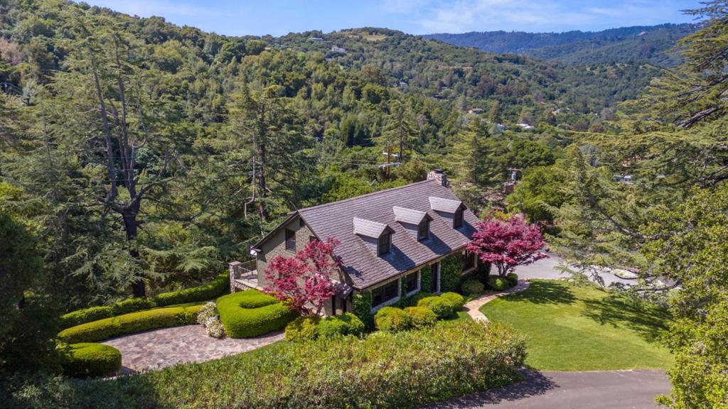 Meticulously cared for over four decades, this one-of-a-kind property sits atop a scenic hill just minutes from downtown Los Gatos. With a striking stone facade built from on-site quarried stone, the home blends seamlessly into its natural surroundings. Set on nearly two acres, the estate, La Deodara, features an expansive lawn shaded by mature trees and panoramic views stretching over Silicon Valley. The interior features two stories of thoughtfully designed living space, including a grand living room with a stone fireplace, built-in library, and large picture windows. The formal dining room leads to a chefs kitchen with a Wolf stove, Subzero fridge, eat-in booth, and stylish finishes. A main-level bedroom and full bath offer a downstairs retreat with south-facing rooms opening to an expansive deck. Upstairs are two spacious bedrooms, a well appointed full bath, and a flexible bonus room. Quality finishes include Connecticut blue stone walkways and designer interiors. Ample parking with attached garage, separate detached garage, and large driveway. A charming detached cottage provides flexible options for guests or work-from-home. Part of Los Gatos history, this peaceful estate is in the top-rated Los Gatos school district and offers stunning views, privacy, & timeless character