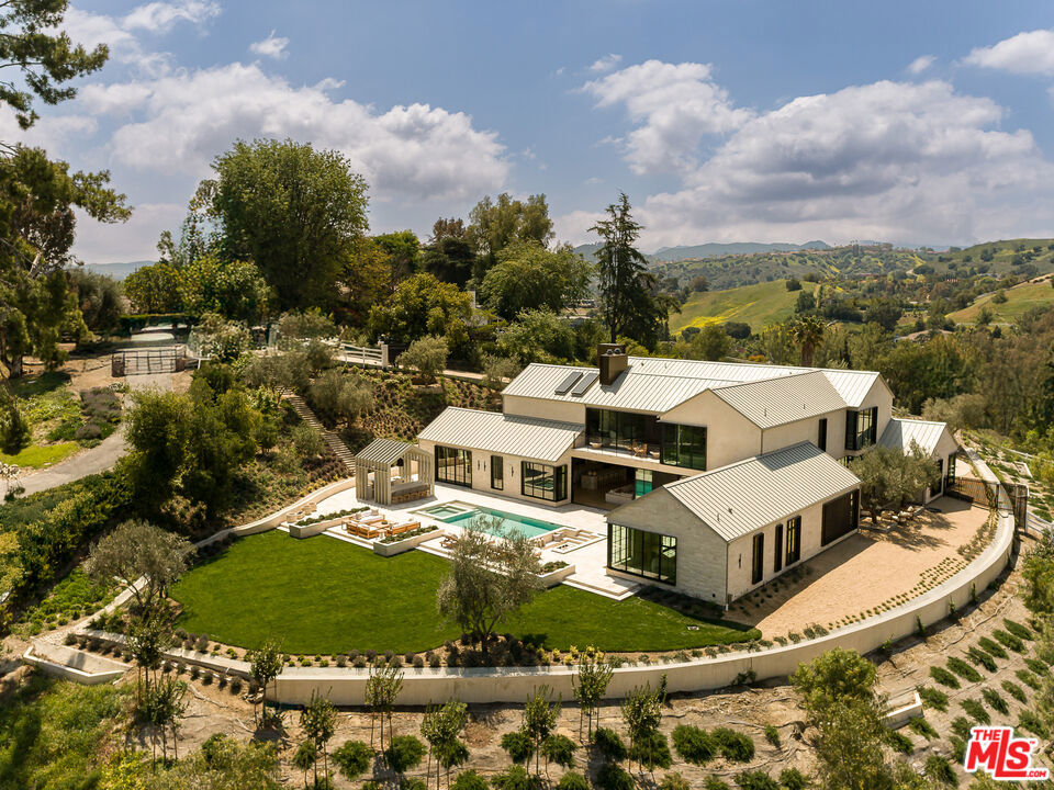 Introducing 24172 Lupin Hill Road, A modern chalet hidden in the hills of California. Unveiled as a paragon of contemporary architecture and refined design, 24172 Lupin Hill Road emerges as a newly constructed estate nestled within the prestigious, guard-gated community of Hidden Hills. An inspired collaboration of design and craftsmanship, this nearly 11,000-square-foot estate with a 4-car-garage is a rare offering that captures the essence of luxurious interiors and the laid-back beauty of California living. Set behind grand double gates and approached by a long, private driveway framed by majestic landscaping and a roundabout motor court, this architectural tour de force is the epitome of seclusion and elegance. Every inch of the home speaks to intentional design and elevated living. Inside, a vast open floor plan unfolds beneath soaring ceilings, blending form and function with the use of natural stone, organic textures, and exquisite custom finishes throughout. Anchoring the estate is an oversized dedicated dining area, perfect for hosting grand-scale gatherings, and a striking library-office pairing that redefines luxury work-from-home environments. A four-car garage offers ample room for collectors and convenience, while the wellness wing transports residents into a sanctuary of rejuvenation. Here, a spacious wellness and fitness room complemented by a cold plunge stone tub beneath the open sky, inviting daily rituals of health and vitality. The primary suite is a true sanctuary featuring dual walk-in closets of generous scale and a spa-worthy bathroom that rivals the finest hotels, complete with a sculptural stone soaking tub oriented toward sweeping canyon and hillside views. For ultimate functionality and guest privacy, a beautifully appointed poolside guest house expands the estate's living quarters, ideal for hosting in effortless style. Indoor and outdoor boundaries dissolve as walls of glass frame the estate's manicured grounds, where curated landscape design meets breathtaking natural surroundings. Every detail from materiality to flow has been crafted to offer an immersive living experience that is both grounded in nature and boldly luxurious. More than a residence, 24172 Lupin Hill Road is a private sanctuary, a design statement, and a legacy in the making a new benchmark for the traditional-modern living in Hidden Hills.