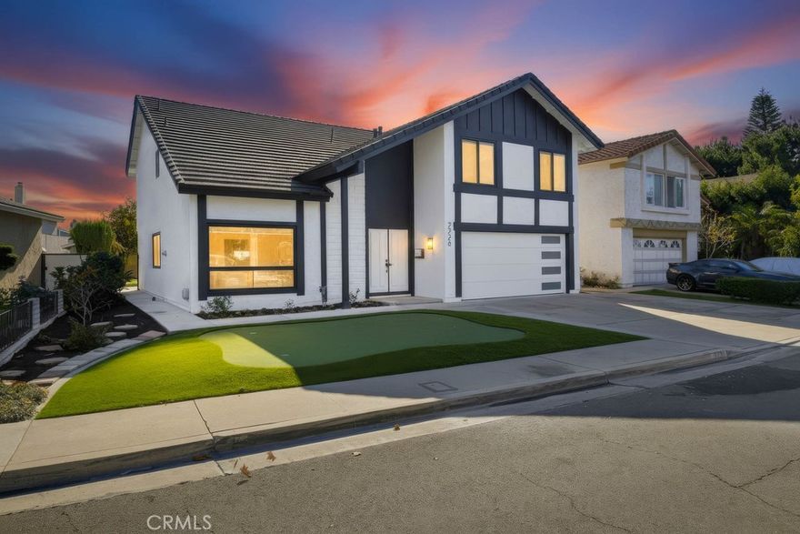 Located on a quiet Anaheim street, this updated home offers clean curb appeal with a white exterior, black trim, and a neatly landscaped front lawn. Inside, wood floors and an airy, open layout create a bright and welcoming first impression. The main living area features high ceilings, recessed lighting, and a large front window that fills the space with natural light. Nearby, the dining area showcases a sleek black metal light fixture and open sightlines to the staircase with modern black railings, setting the tone for the home's contemporary aesthetic. Toward the back of the home, a second expansive living space connects seamlessly to the updated kitchen. This room features a striking dark stone fireplace as its focal point, with sliding glass doors and a full wall of windows providing abundant natural light and backyard views. The kitchen offers white cabinetry, marble countertops and backsplash, black fixtures, and an open layout with space for a breakfast table or additional dining area. A dedicated laundry area and a convenient half bath complete the downstairs level. Upstairs, the hallway includes built-in cabinetry and leads to multiple rooms branching in different directions. A spacious bonus room serves as a flexible playroom or additional living space, enhanced by recessed lighting and large windows. The primary suite includes an updated ensuite bathroom and a walk-in closet. Three additional well-sized bedrooms provide ample accommodation, while a bright, modern full bathroom with white finishes and black accents serves the secondary rooms. The backyard offers a wide, open layout with both hardscape and a crisp grassy lawn ideal for play, entertaining, or future customization. Overall, this home stands out with its modern updates, cohesive black-and-white design elements, abundant natural light, and multiple living spaces designed for comfort and versatility.