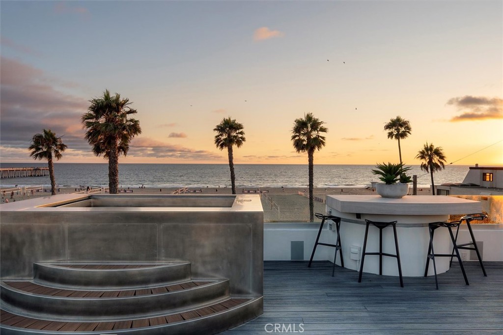 Perched in the heart of Hermosa Beach, just steps from the sand, this home offers an extraordinary coastal lifestyle with panoramic ocean views and unmatched privacy—no neighbors on two sides. This rare offering is ideally situated west of Hermosa Avenue on a premier street, where the sights and sounds of the Pacific are your everyday backdrop. The home unfolds across three beautifully designed levels, all serviced by a private elevator and oriented to maximize the jaw-dropping views stretching from Palos Verdes to Malibu. Wide plank oak floors add warmth and coastal sophistication throughout, while the remodeled kitchen is a dream—equipped with top-of-the-line appliances, dual drink refrigerators, breakfast bar seating and access to a charming patio perfect for morning coffee. The main living area is anchored by an inviting fireplace and expansive windows that frame the horizon, opening to a generous deck with ample space for outdoor dining and entertaining. A spectacular rooftop deck showcases sweeping views of the beach, complete with a stainless-steel spa, outdoor kitchen and bar seating for enjoying the sunset. The primary suite is a serene retreat with its own fireplace and private patio. The en-suite bathroom features a soaking tub, custom tile work, and designer finishes. A private guest suite with its own entrance and laundry area occupies the lower level, ideal for extended family or visiting friends. Smart lighting, motorized window shades, and a thoughtfully open layout elevate the ease and enjoyment of everyday living. Enhancing the experience further is a fully integrated Crestron home system allowing seamless orchestration of your home’s environment and its connection to the outside world. Real-time status updates on your mobile device confirm door locks, alarms, garages, and live camera views—delivering control, security and peace of mind at your fingertips. A two-car garage plus an additional parking space complete the offering. With one of the best addresses in Hermosa Beach, this home captures the essence of beachfront living—unparalleled views, stylish comfort, and effortless elegance by the sea.