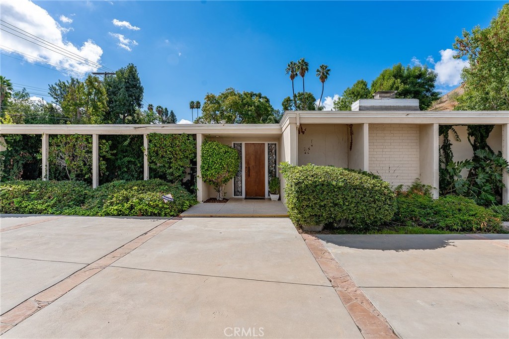Rare opportunity to customize a stellar single story Mid-Century pool home located on a quiet cul-de-sac South of the Boulevard on a sprawling 15,000 SF parcel. The property sits elevated above the street on a sweeping corner lot with wide circular driveway that can accommodate parking for large gatherings plus there is an attached 2-car garage with direct access. Original latticed decorative grid walls and a terrazzo tiled front patio greets you before stepping inside. The entry foyer has convenient guest powder bathroom and is positioned perfectly dead center to the backyard with large glass slider that immediately beckons you to the pool and the grounds beyond. The home uniquely wraps around the backyard in a U-shaped fashion which floods the home with natural light and allows all interior spaces to overlook the backyard. An oversized living room boasts high tongue and groove wood beamed ceilings found throughout the home, stunning stone fireplace with terrazzo tiled hearth, walk-in bar with pass through serving counter to the yard, and two sets of glass sliders that open to the exterior. Formal dining room has custom built-in buffet counter with terrific storage cabinetry and large picture window. The spacious kitchen opens to all living spaces and features peninsula with bar top seating, ample cabinetry with multiple pantries, Thermador stovetop, and double ovens. A separate den off the kitchen features brick fireplace flanked by built-in shelving and two sets of glass sliders that open to the covered patio. A separate adjacent office or guest room has access to its own bathroom. The grand primary suite has two sets of glass sliders that open to the backyard, large walk-in closet with additional wall-to-wall wardrobe closets, and en-suite bathroom with dual sinks, walk-in shower, and separate spa tub. Two well appointed secondary bedrooms share a sizable hall bathroom. Separate laundry area with storage has side yard access. The entertainer’s backyard is designed around an oval shaped swimming pool with two outdoor changing rooms, large covered patio ideal for outdoor dining, and separate flat pad with endless possibilities - outdoor kitchen, fire pit, lawn for play, you name it. Fantastic opportunity to reimagine your mid-century dream home.