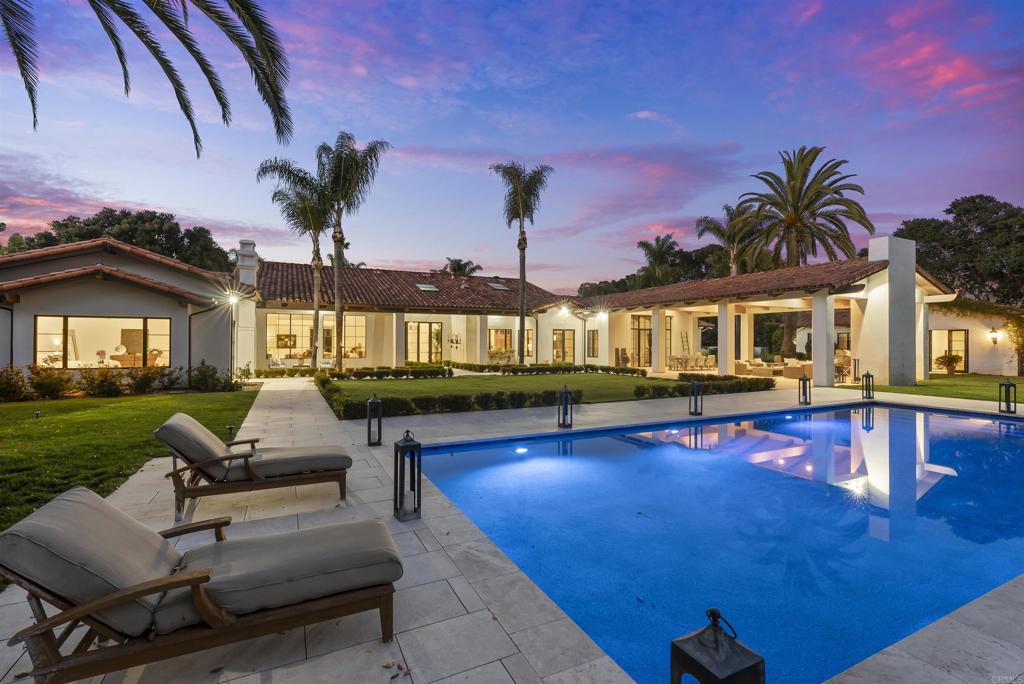 Privately gated within the prestigious Rancho Del Lago community, this 4-acre modern Mediterranean estate offers timeless design and refined living in Rancho Santa Fe. The nearly 8,000 sq ft single-level home features a flowing open-concept floor plan with light-filled interiors, generous en-suite guest bedrooms, dual offices, and a luxurious primary suite with spa-like bath, fireplace, and dual walk-in closets. A detached 1BR/1BA guest house provides private accommodation for extended stays. The gourmet kitchen is outfitted with Subzero, Wolf, and Miele appliances and opens to spacious living and dining areas that overlook the tranquil outdoor setting. A grand loggia with statement fireplace anchors the resort-style backyard, complete with a pool, putting green, bocce court, garden beds, and lush landscaping with over 140 orange trees. Set on 4 acres, the estate offers ample versatility and opportunity for a future owner to create their dream estate whether that be adding a tennis court, sport court, ADU, equestrian facilities, or whatever one’s heart desires. Here, the possibilities are endless. Equipped with owned solar, backup generator, and a private well, this estate blends beauty, function, and convenience —just minutes from the Village, Roger Rowe School, golf, and the coast.