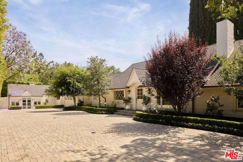 Tucked discreetly behind a wrought-iron gate and up a long, picturesque driveway that crosses a charming bridge, this beautifully reimagined ranch-style retreat offers a rare blend of privacy and allure. Sheltered beneath a canopy of oak trees and framed by vibrant rose gardens, the home exudes warmth and sophistication. Meticulously remodeled with high-end finishes and an exceptional eye for detail by interior designer Paula Bruss, the single-story residence is filled with natural light, thanks to expansive windows that capture the sun from dawn to dusk. Vaulted ceilings, refined stone and tile work, designer fixtures, and architectural character elevate every room with timeless charm. French doors open to an enchanting backyard oasis, with a spectacularly oversized swimming pool and lush green lawn perfect for relaxing, entertaining, or simply enjoying the serenity of nature. The long paver-stone driveway leads to a spacious motor court with ample parking, in addition to a two-car attached garage. A separate, private guest house complete with a full bathroom and kitchenette offers ideal accommodations for guests, extended family, or a home office. The main residence includes three bedrooms (one of which is currently converted into a custom closet but can be easily reverted), spanning approximately 3,770 sq ft. The guest house adds an additional approximate 400 sq ft of well-appointed living space.