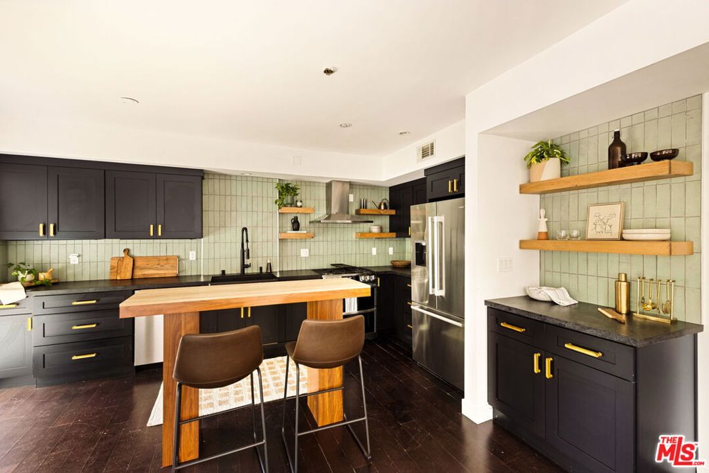 This stunning condo that vibes like a townhome perfectly combines a slice of modernism with luxury. Floor to ceiling windows bring in a bunch of natural light into this open floor plan with nicely contrasted dark wood floors. Sizable living room opens into the remodeled kitchen with stainless steel appliance portfolio, wood cabinets and stone countertops accented with gold fixtures and a mint green tiled backsplash. Two large bedrooms with a third bedroom uniquely designed for an office space or playroom. Primary bedroom offers an ensuite bathroom with mosaic tile and modern finishes. Second bathroom has a navy blue palette outfitted with terrazzo floors and custom fixtures. Condo has stackable laundry closet and thoughtful details such as remote-operated window shades, Nest thermostat, and a wet-bar for hosting friends. The unit comes with 2 gated tandem and covered parking spots, plus a communal guest spot. Additionally, the dedicated spots were recently wired to be electric vehicle charger ready. In front, enjoy a spacious private patio that's perfect for entertaining and relaxing, set back from the street with a frosted glass gate for privacy and shaded by mature trees and landscaping covered by the HOA. Low monthly HOA fee includes fire and earthquake insurance, no rental restrictions. Close to La Cienega and 10 freeway access. Welcome Home.