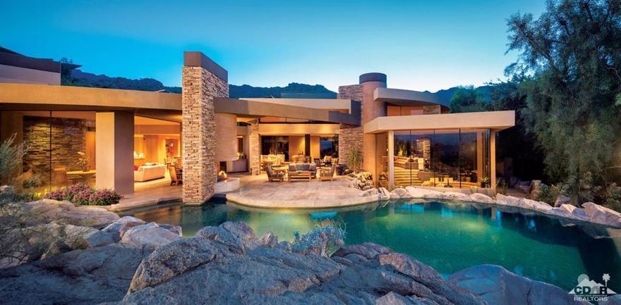 Gold Nugget Award winning home known for its dramatic architecture. Artistic glass, stainless steel custom gate opens to a bridge rock way with water feature, double glass entry doors leading to inside's expansive floorplan. Guy Dreier designed with floor to ceiling glass in every direction. The location sits elevated in the foothills of BIGHORN's mountain estates and offers stunning mountain range and down-valley vistas. Perfect home for desert entertaining offering an open and spacious living room w/intimate seating and conversation areas, two-sided curved fire&ice fireplace, glass pocket sliders allow seamless transition of indoor/outdoor living, theater, sunken bar and lounge with spectacular views. Office w/bath plus three spacious guest suites and one offers a separate family room w/media center and morning bar. Spacious master suite is a true retreat w/glass sliders opening to private patio w/natural rock outcroppings, spa and outdoor shower. Interior and exterior water features
