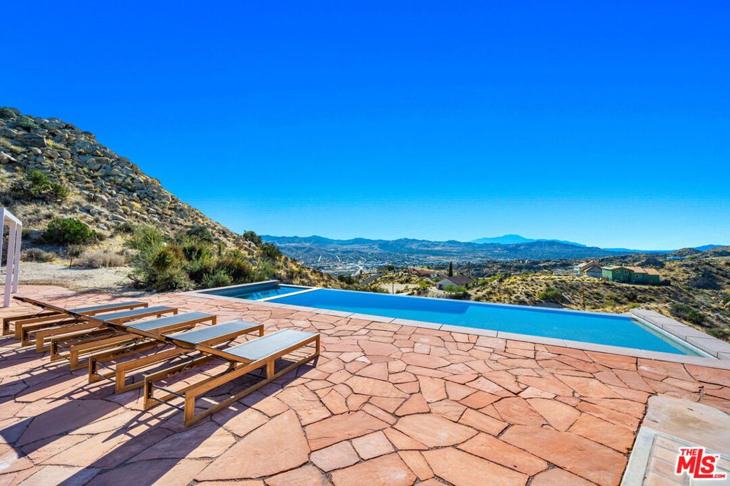 Spectacular 4-Bedroom Desert Estate with Infinity Pool, Panoramic Views & Custom Finishes on 2.5 Acres. Welcome to your private hillside oasisan architecturally distinctive 4-bedroom, 2.5-bathroom home offering approximately 3,400 square feet of beautifully crafted living space, perched on 2.5 acres with unobstructed high-desert and mountain views. This one-of-a-kind property is perfect for those seeking luxury, privacy, and dramatic natural beauty.From the moment you arrive, the gated entry and circular drive set the tone for this custom Spanish-influenced retreat. A tiered fountain anchors the front courtyard, surrounded by low-maintenance desert landscaping and mature native plants. Step through hand-carved double entry doors into a grand living space where vaulted tongue-and-groove ceilings soar overhead and massive picture windows frame jaw-dropping views. A striking stone fireplace serves as the centerpiece of the great room, seamlessly connecting indoor living to the expansive outdoor entertaining areas.Designed for both comfort and entertaining, the open-concept floorplan includes a stunning chef's kitchen with quartz countertops, artisan backsplash tile, custom open shelving, stainless steel appliances, and wraparound corner windows that capture endless desert light. A charming dining nook adorned with three stained-glass arched windows and wood-paneled walls offers an intimate setting for meals with family and friends.The luxurious primary suite features its own private slider to the pool patio, mountain views, and a beautifully designed en-suite bath. Three additional bedrooms provide ample space for guests, a home office, or creative use. Throughout the home, you'll find curated finishes including handcrafted lighting, vintage tile, wood floors, and rustic design details that enhance the home's warm and welcoming character.The resort-style backyard is the crown jewel of the property. An infinity-edge pool and spa appear to spill directly into the horizon, while the flagstone pool deck offers multiple lounge areas, fire pit, and a setting unlike any other. Whether you're hosting sunset gatherings or enjoying serene morning coffee with a view, this space is designed to inspire.Other highlights include a detached bonus structure (perfect for a studio or guest use), ample parking, and proximity to hiking, downtown amenities, and Joshua Tree National Park.