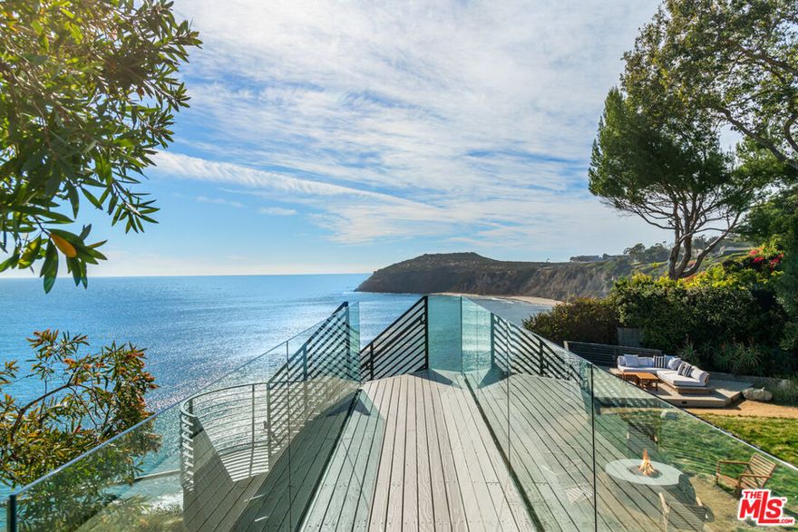 Commanding an unobstructed panorama of sky and sea, this gated Point Dume contemporary estate with Riviera 3 beach key is magnificently sited on a bluff-front property of more than an acre and exquisitely updated for recreation, relaxation, and impressive entertaining. Every aspect of the interior and exterior design and landscaping emphasizes the home's architectural beauty, tranquil comfort, and gorgeous views. From the motor court, a walkway and ramp overlook the serene front gardens. This spacious and very private sanctuary features a heated swimming pool and brand-new Jacuzzi with an enormous new wood deck, a new firepit, and an outdoor kitchen complete with a barbecue, pizza oven, ice machine, sink, and small fridge. The home's top floor formal entry reveals the dramatic open floor plan, high ceilings, glossy hardwood floors, and views, views, views. The living/dining great room has a central round fireplace, large greenhouse-inspired windows on one side, and a wall of glass on the other, opening onto a glass-railed entertainer's deck that runs the full width of the house. The adjoining gourmet kitchen is fully refurbished, with an eat-in counter that is open to the dining area, pass-through windows to the deck, and stunning ocean views. This level has been opened to feature a spacious family room with a fireplace, flat-screen TV, and ocean views. Also on this level is a powder room with a shower. The deck extends to a partially covered floating walkway and steps down to the very private backyard with sweeping ocean views, a wood patio for al fresco dining and relaxation, and a fire pit with a seating area. Stairs from the formal entry lead to the lower level, where there is access to the front yard and pool, plus four ocean-view bedrooms. These include the spacious owner's suite, with high ceilings, a wall of closets, flat-screen TV, a sensational, newly refurbished bathroom, and glass doors to an ocean-view Jacuzzi, a full-width wood deck, the grassy yard, and the bluff front with amazing ocean views. Beautifully landscaped in a style that is both manicured and natural, every step of the backyard highlights the view, with a path that meanders from one seating area to another. At the front of the house is a three-car garage guesthouse with an exceptionally spacious and comfortable tiered home theater with surround sound and a kitchenette on the lower level. Upstairs is a spacious guest suite with a living room, dining area, and full kitchen. Additional features include ample guest parking, a 60-foot regulation bocce court, a Control 4 system for interior and exterior lighting and sound, as well as 38 370KW solar electric panels, plus 14 hot water solar panels to heat the pool. This estate is Malibu beachfront comfort at its finest.