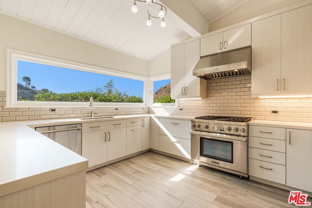 Perched on a large 10,567 sq ft lot atop a peaceful knoll, this light and bright single-story home offers privacy, charm, and peace of mind with no surrounding homes impacted by recent fires and full post-fire remediation completed. Inside, a spacious entry with atrium and fountain opens to a living and dining room with vaulted ceilings, sunlit windows, and a cozy fireplace. The fully remodeled gourmet kitchen, featuring granite countertops, a breakfast bar, and an adjacent family room with a fireplace, makes for an ideal gathering space that flows seamlessly to the outdoors through numerous French doors. Freshly painted throughout, the home features three bedrooms, a bonus room, and two and a half baths, including a primary suite with a walk-in closet, en-suite bath, and direct patio access. Outdoors, newly landscaped gardens with walking paths, sitting areas, and peek-a-boo ocean views complement the expansive lawn. With excellent curb appeal, natural light, and direct access from the attached two-car garage, this move-in-ready property is truly a gem.
