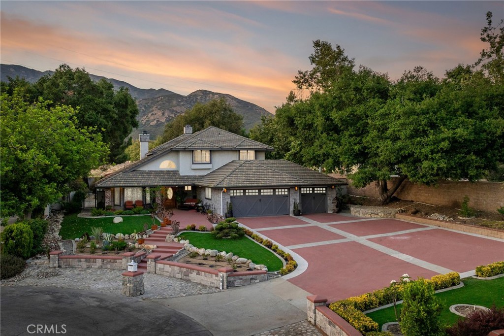 Blaisdell Ranch | Prime End-of-Cul-De-Sac Estate with Expansive Views & Entertainer’s Backyard.
Tucked away at the end of a quiet cul-de-sac in the coveted Blaisdell Ranch community, this exceptional residence sits on a deep, private lot framed by mature landscaping, extensive stonework, and a stately oak tree that anchors its elegant curb appeal. An oversized driveway and a welcoming covered front porch set the stage for the refined living spaces within. Step through the front door to a tiled entryway that opens to a formal living room with a beveled glass bay window and tile flooring. Just beyond, a family room impresses with a towering floor-to-ceiling fireplace, recessed lighting, and opens to a sunken lounge, a warm and inviting space featuring a built-in wet bar with stone counters, a comfortable sitting area, and arched windows framing serene mountain views. The remodeled kitchen is a showpiece, designed with rich cherrywood cabinetry, granite countertops and backsplash, stainless steel appliances, a center island, and an eye-catching double tray ceiling with recessed lighting. The adjacent breakfast nook is surrounded by windows and topped with a matching tray ceiling, bathing the space in natural light. A formal dining room with a recessed, coffered ceiling and chandelier provides an elegant setting for entertaining. A charming brick-floor bonus room offers the perfect transition to the backyard, accessible through a sliding glass door. The main level also features a private office, a bedroom, a ¾ bathroom, and a spacious laundry room with direct access to the three-car garage. Upstairs, the expansive primary suite is a true retreat, offering a brick fireplace and French doors that open to a large private balcony with panoramic views. The remodeled ensuite bath features dual vanities with stone countertops, a dedicated makeup station, a soaking tub framed by shuttered windows, a walk-in shower, and a generous walk-in closet. Two additional upstairs bedrooms share an updated hall bathroom. The backyard is a park-like sanctuary, professionally landscaped with meandering paver walkways, vibrant greenery, and a central lawn surrounded by curated garden beds. Entertain effortlessly with a koi pond, multiple seating areas, and a built-in barbecue under a covered pergola, perfect for dining al fresco. With no rear or side neighbors, full block privacy walls, and lush natural screening, this outdoor space offers seclusion and tranquility.