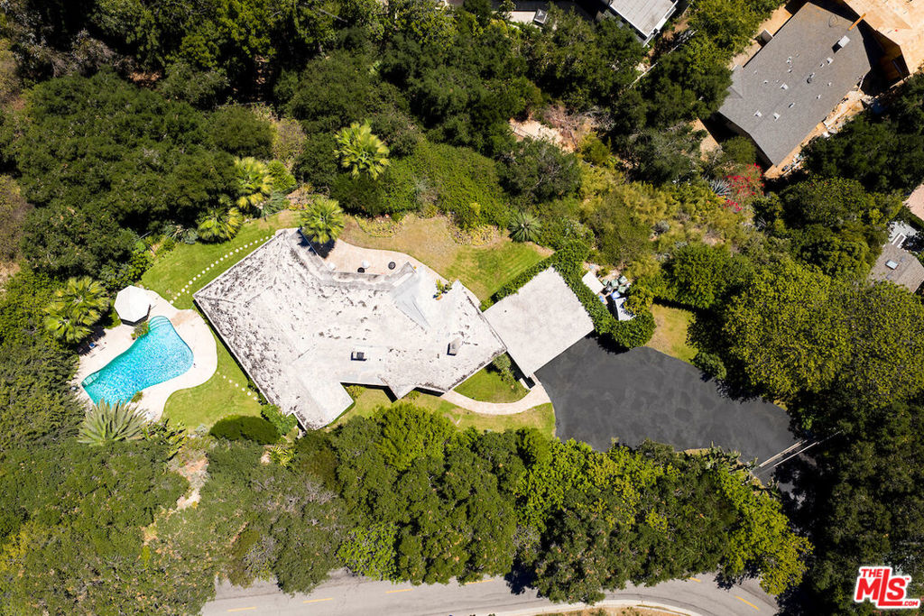 Mid-century gem privately tucked behind gates on a sprawling 1.4-acre lot in Bel Air with exceptional views from the city skyline to the Pacific Ocean. Wood-carved double doors lead into the expansive living room lined with vaulted ceilings and concrete flooring, paying homage to true mid-century design along with the stone fireplace. Wall-to-wall glass sliding doors harmoniously blend indoor-outdoor living, providing access to the patio for dining al fresco, and flood the interior with natural sunlight throughout. A chef's kitchen, dining room, and four bedrooms with updated en suites complete this functional floor plan. A stone pathway, framed by lush greenery, leads to the expansive in-ground pool with an abundance of lounging areas to enjoy this tropical oasis. An oversized motor court plus a three-car carport ensure ample parking. Seldom does a property offer land and views in one of the most highly coveted locations in Los Angeles while also providing an opportunity to reimagine for value add.