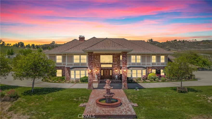 Nestled in the heart of Temecula’s prestigious Wine Country, this extraordinary vineyard estate is a celebration of refined living, panoramic beauty, and the art of winemaking. Set high on the hilltop, this residence overlooks your very own working vineyard, flourishing with Cabernet, Syrah, Merlot, Muscat, Petite Syrah, and Primitivo varietals—an exceptional opportunity to embrace the vintner lifestyle. Step through a grand single entry into a world of timeless elegance. The dramatic foyer welcomes you with two breathtaking chandeliers, a gracefully curved staircase, and vaulted ceilings adorned with rich wood beams, all bathed in natural light. Thoughtfully designed for both comfort and sophistication, the home features a chef’s dream kitchen—ideal for gatherings both intimate and grand—alongside an expansive bar and open-concept living spaces that flow effortlessly throughout. A beautifully customized library/office on the main floor offers a quiet retreat, complete with rich wood shelving and fine craftsmanship. The layout includes a spacious downstairs bedroom with a full bathroom, perfect for guests or multi-generational living, along with an elegant powder room for visitors. Upstairs, a square catwalk offers sweeping views into the magnificent great room below and leads to four generously sized bedrooms, each filled with natural light and designed for comfort. The primary suite is a true sanctuary—boasting serene views of the vineyard, a cozy sitting retreat with fireplace, and a spa-like ensuite bath. Enjoy a luxurious soaking tub, walk-in shower, dual vanities, and a large walk-in closet, all creating the ultimate place to unwind. A secondary dwelling above the detached garage currently serves as a private winemaking room, but offers endless potential as a guest suite or creative space. Every detail of this home exudes luxury, privacy, and lifestyle. Whether you envision a boutique wine label, a family estate, or an entertainer’s dream, 37028 De Portola Road delivers the very best of Temecula Wine Country living.