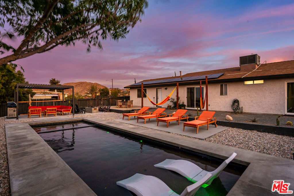 Welcome to your private desert oasis. This beautifully updated 3-bedroom, 2-bathroom home is sited on a spacious and fully fenced -3/4 acre lot, offering resort-style amenities and modern comforts just minutes from downtown Joshua Tree and the National Park entrance. The outdoor living space is ideal for both entertaining and relaxation, featuring a 25-foot in-ground pool/spa with Baja shelf, a shaded pergola with BBQ and dining area, a built-in fire pit with seating, two hammocks, and multiple lounge zones all framed by open desert skies and privacy fencing. Inside, the open-concept layout includes a gourmet kitchen with stainless appliances, an inviting living area with electric fireplace, and smart TVs in every bedroom. This property has a strong track record as a short-term rental. Whether you're seeking a primary residence, vacation home, or income-producing investment, this home delivers the ideal balance of style, functionality, and location in the heart of Joshua Tree.