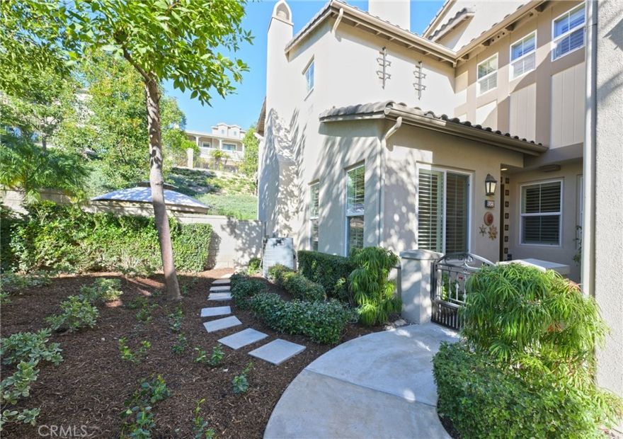 Welcome to luxury living in the prestigious San Lorenzo community of Yorba Linda. This fabulous single-level corner-unit townhome offers 1,702 square feet of beautifully appointed living space, three bedrooms, two-and-a-half bathrooms, and an attached two-car garage. The interior features luxury vinyl plank flooring and plantation shutters throughout, creating a warm and sophisticated atmosphere. The stunning gourmet kitchen features granite countertops, a large island with bar seating, stainless-steel KitchenAid appliances, including a five-burner cooktop, LED recessed lighting, and an abundance of cabinetry. The kitchen opens to an inviting family room enhanced by high ceilings and a charming gas fireplace with logs. The dining room offers high ceilings and a new chandelier. The spacious primary bedroom features an elegant arched window and leads to a luxurious primary bathroom appointed with dual sinks, Corian countertops, a tile backsplash, a large wall-sized mirror with upgraded fixtures, a soaking tub, a frameless glass shower, and a generous walk-in closet with a chandelier. The secondary bedrooms are equally inviting, offering high ceilings and mirrored closet doors. The hall bathroom includes a tub/shower combination with Corian countertops, while the powder room provides a pedestal sink and updated fixtures. Additional conveniences include an inside laundry room with built-in cabinetry and a two-car garage with epoxy flooring and a workbench area. A spacious backyard space with updated landscaping includes a lemon tree and a newer gazebo. Recent upgrades completed in 2020 include the water heater, interior paint, flooring, baseboards, kitchen faucet, garbage disposal, several appliances, and refreshed backyard landscaping—enhancing both comfort and curb appeal. HOA amenities include a swimming pool, spa, and clubhouse. This exceptional property offers upscale living in a serene community close to shopping, dining, and award-winning schools.